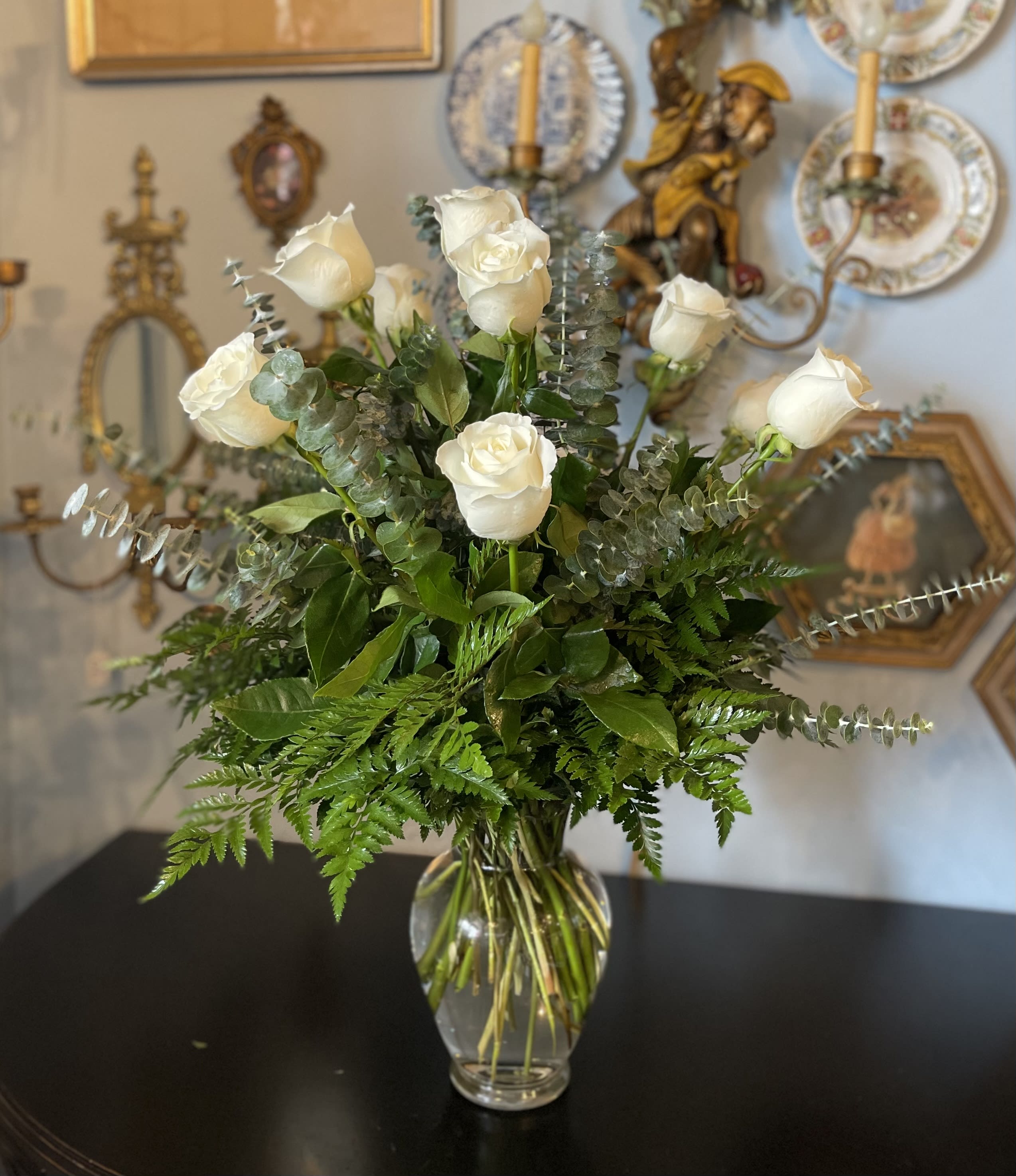 White roses arranged in a clear glass vase with greenery