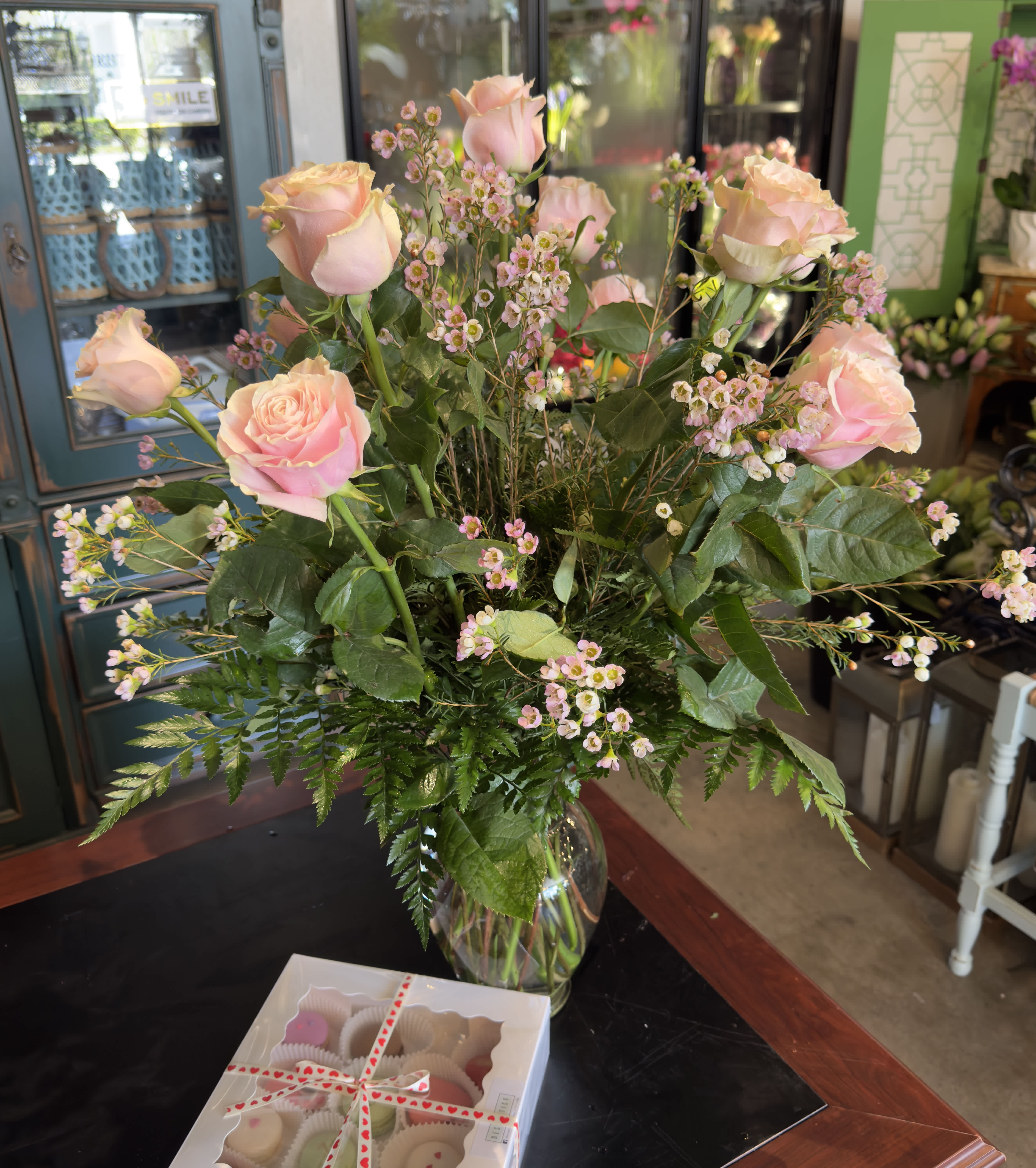 Pink roses and tiny pink filler flowers in a glass vase with a box of chocolates