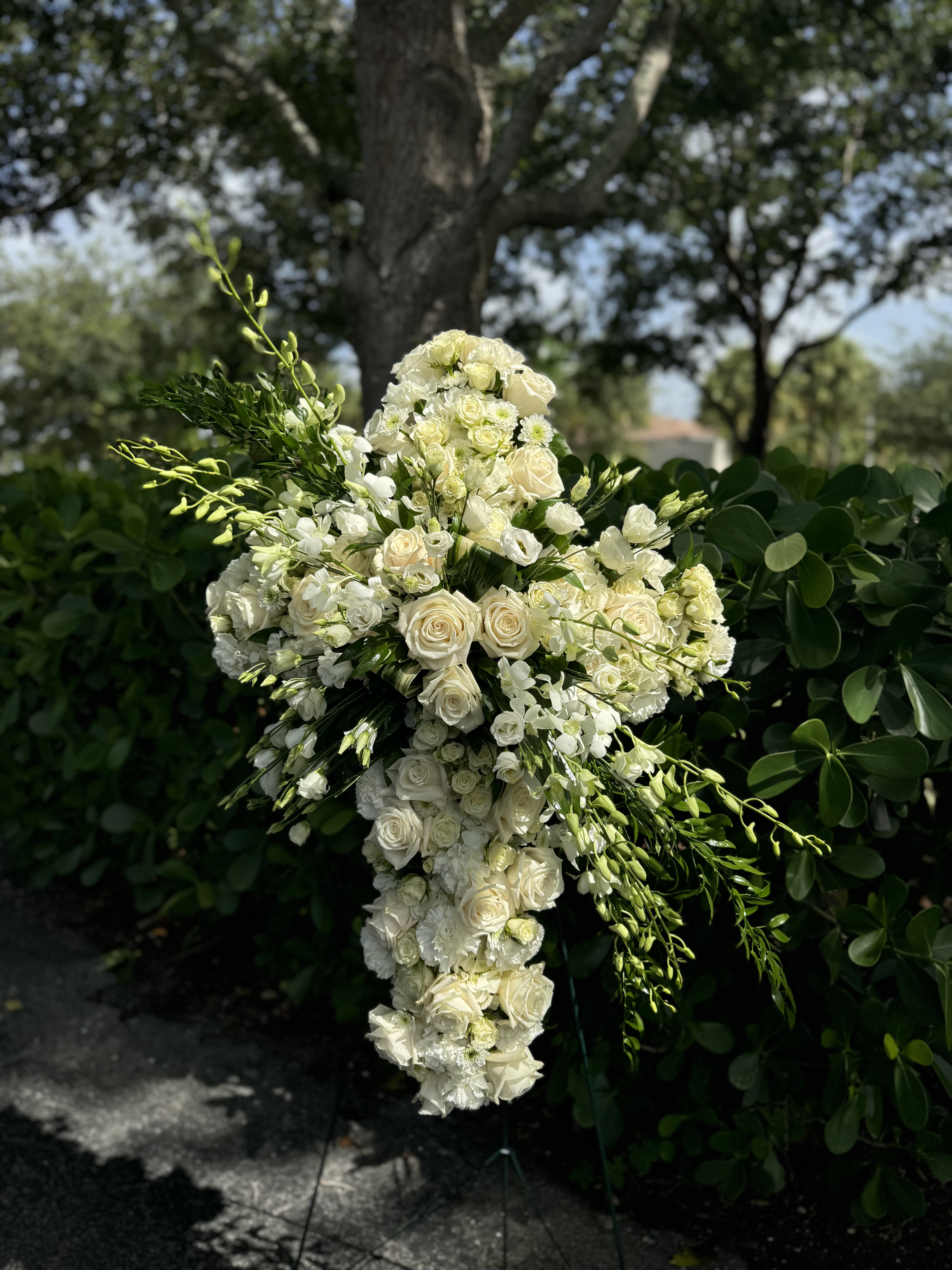 White floral cross-shaped arrangement with roses and orchids
