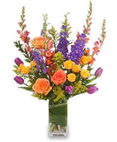 Colorful bouquet of roses, tulips, and purple spikes in a glass vase