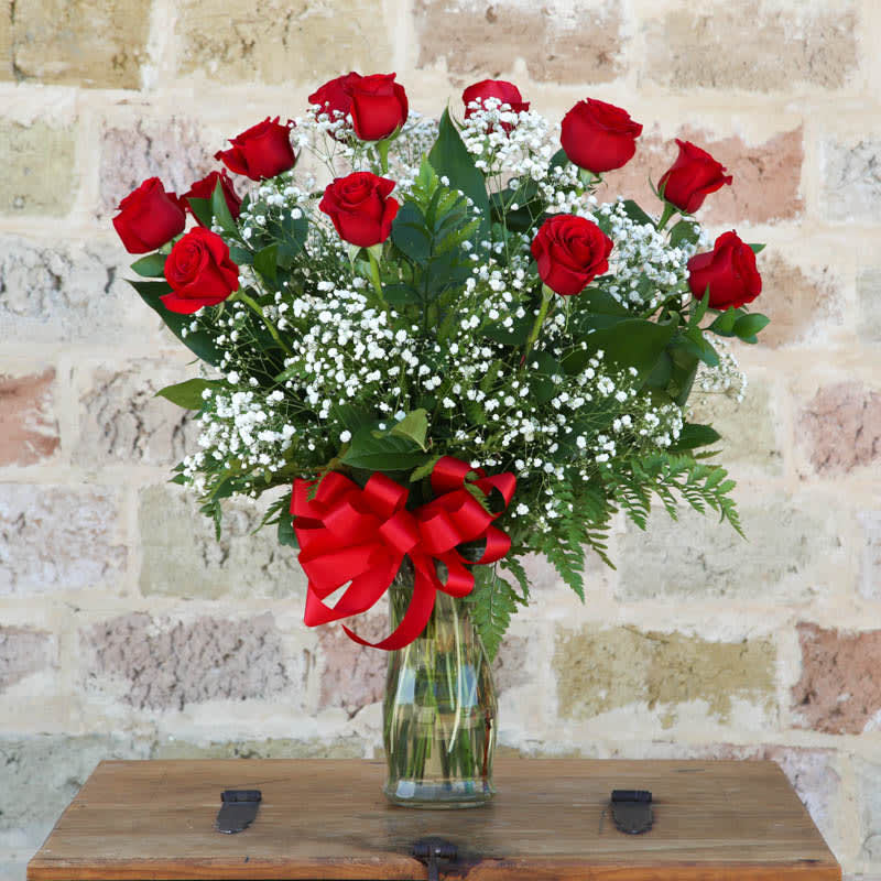 Red roses and baby's breath in a glass vase with a red ribbon