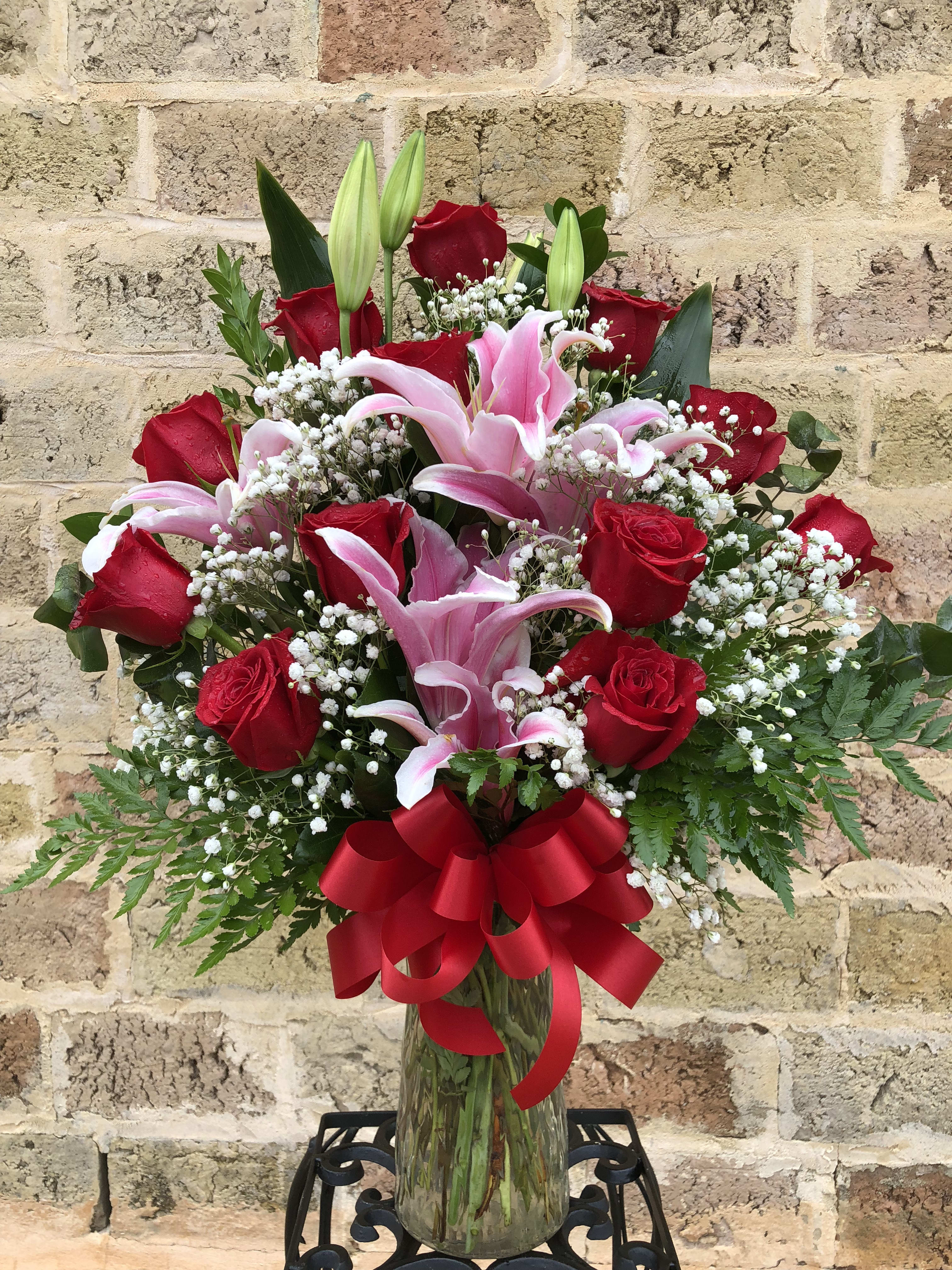 Red roses and pink lilies in a glass vase with a red ribbon