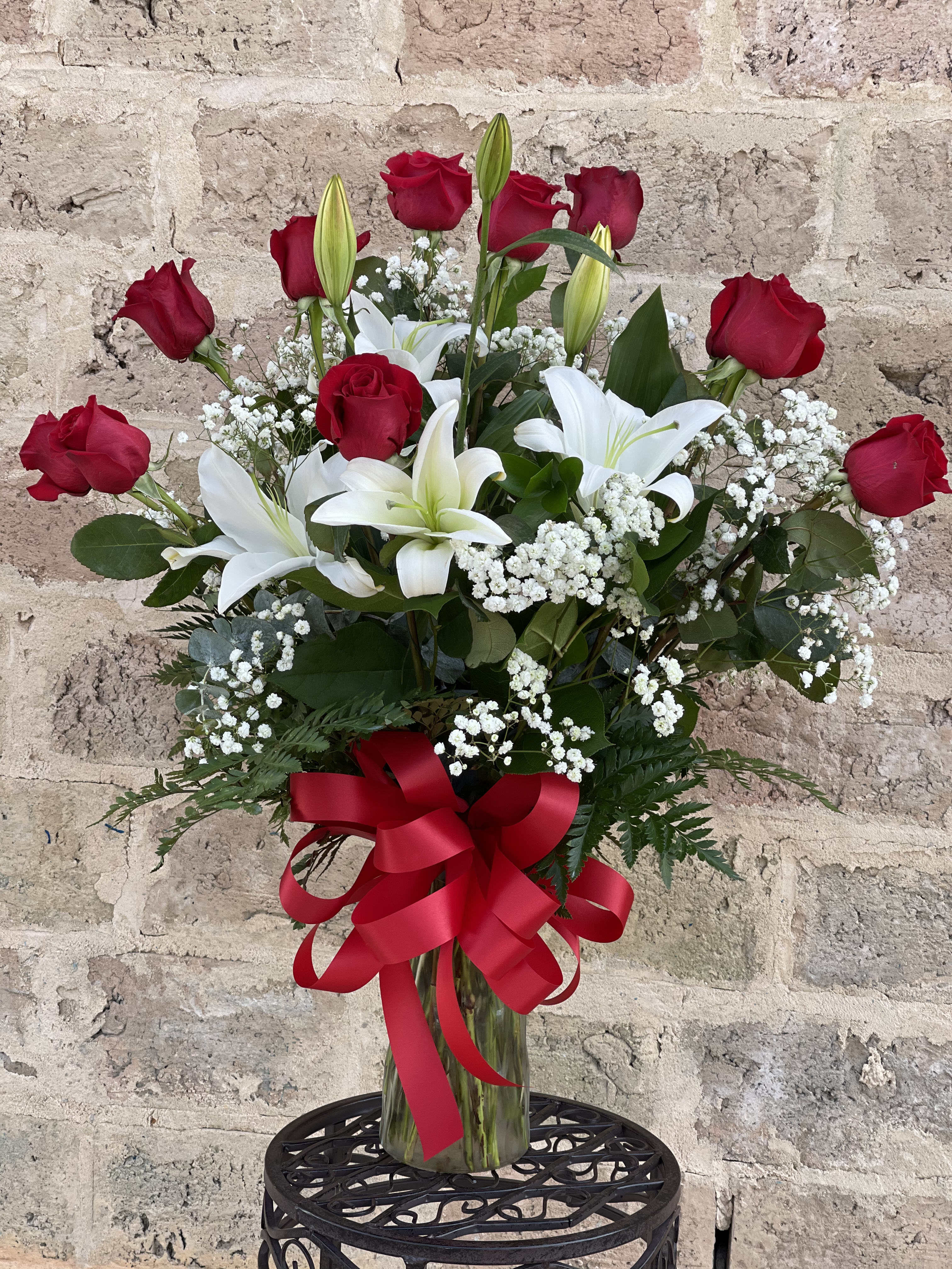 Red roses and white lilies in a clear glass vase with a red ribbon