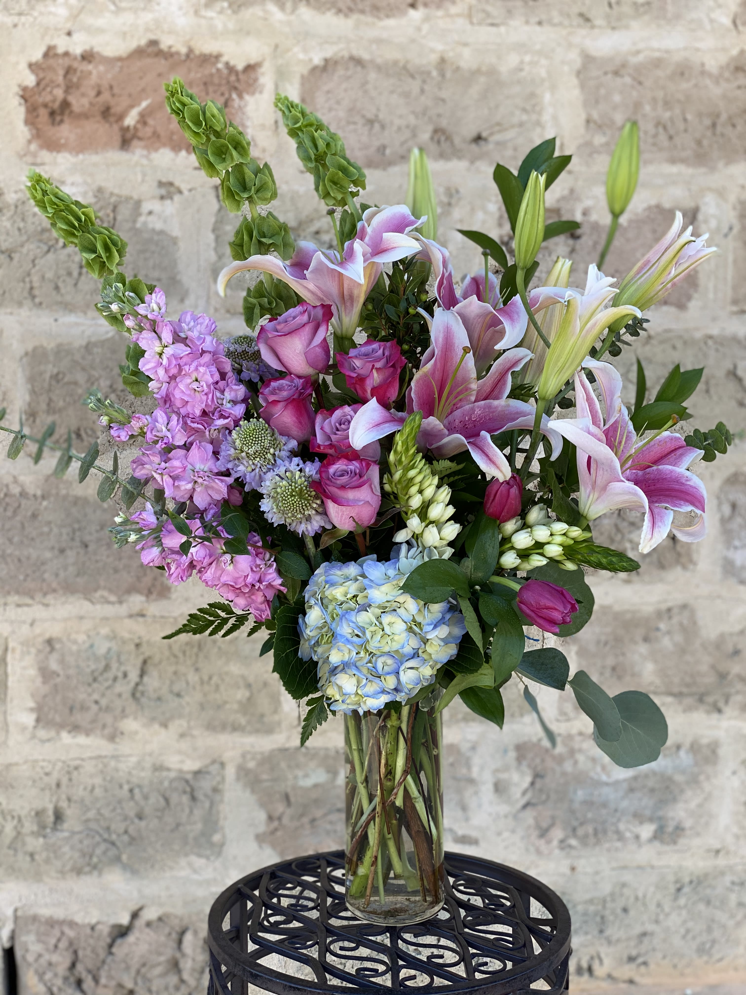 Mixed bouquet of pink lilies, roses, hydrangea, and lavender flowers in a glass vase