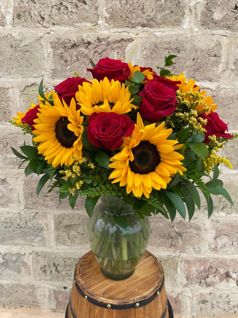Bouquet of red roses and yellow sunflowers in a glass vase