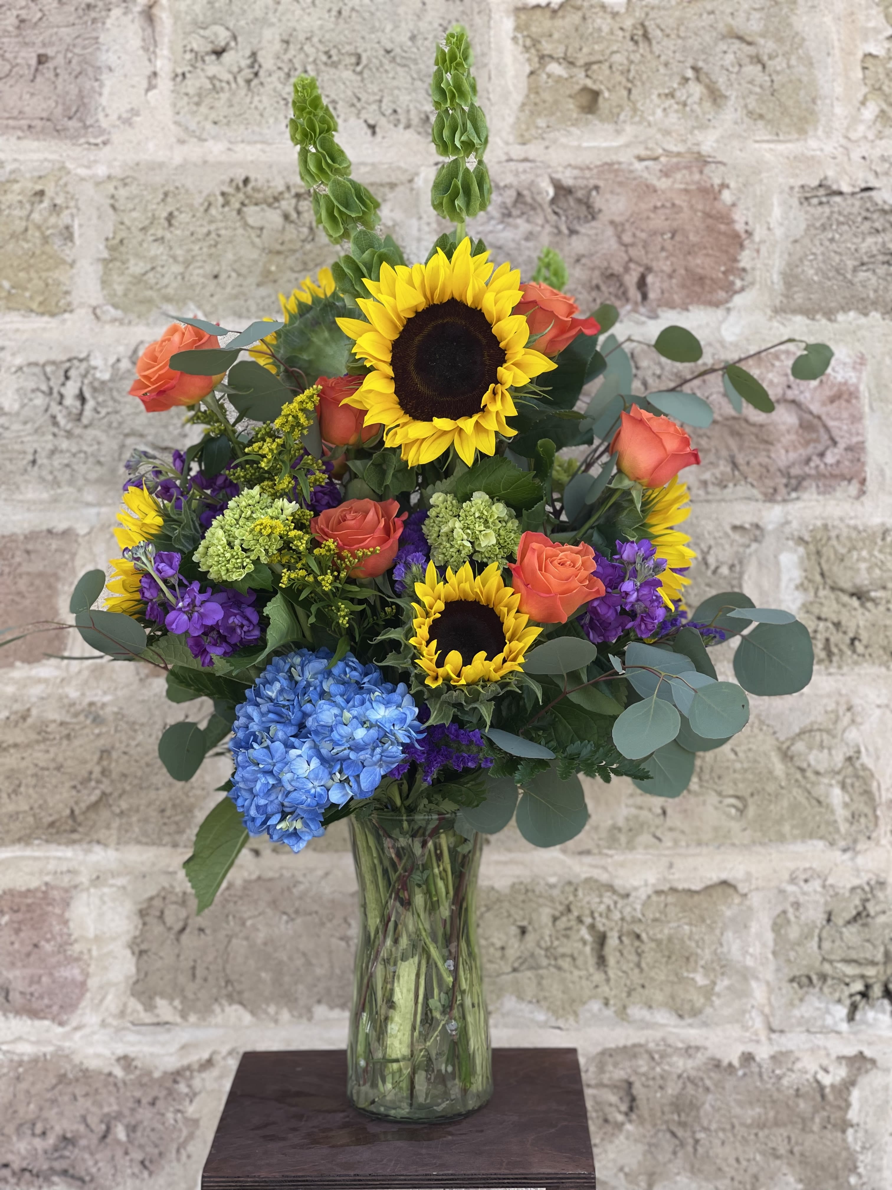 Mixed bouquet with sunflowers, orange roses, and blue hydrangea in a glass vase