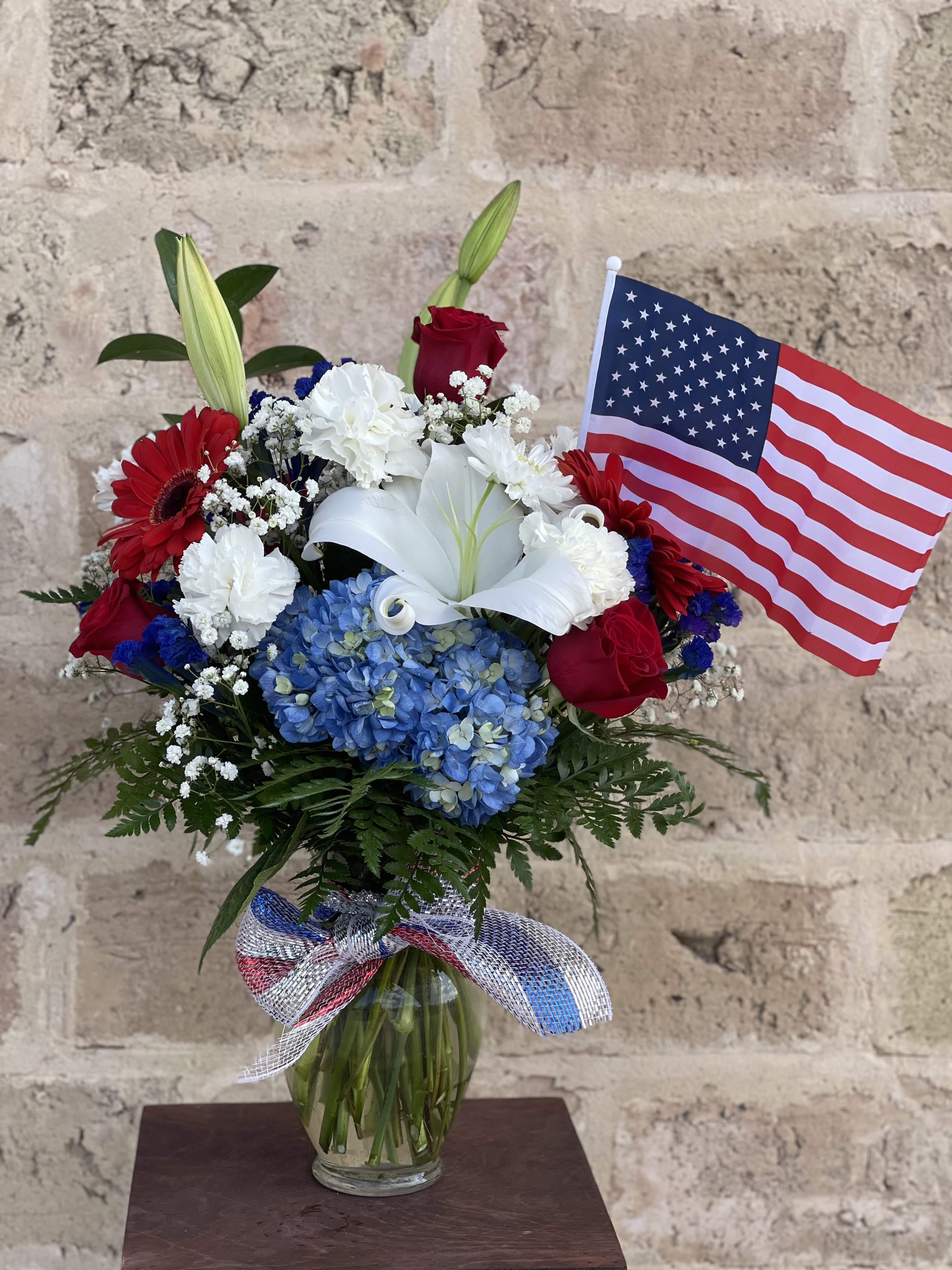 Bouquet of red, white, and blue flowers in a glass vase with an American flag