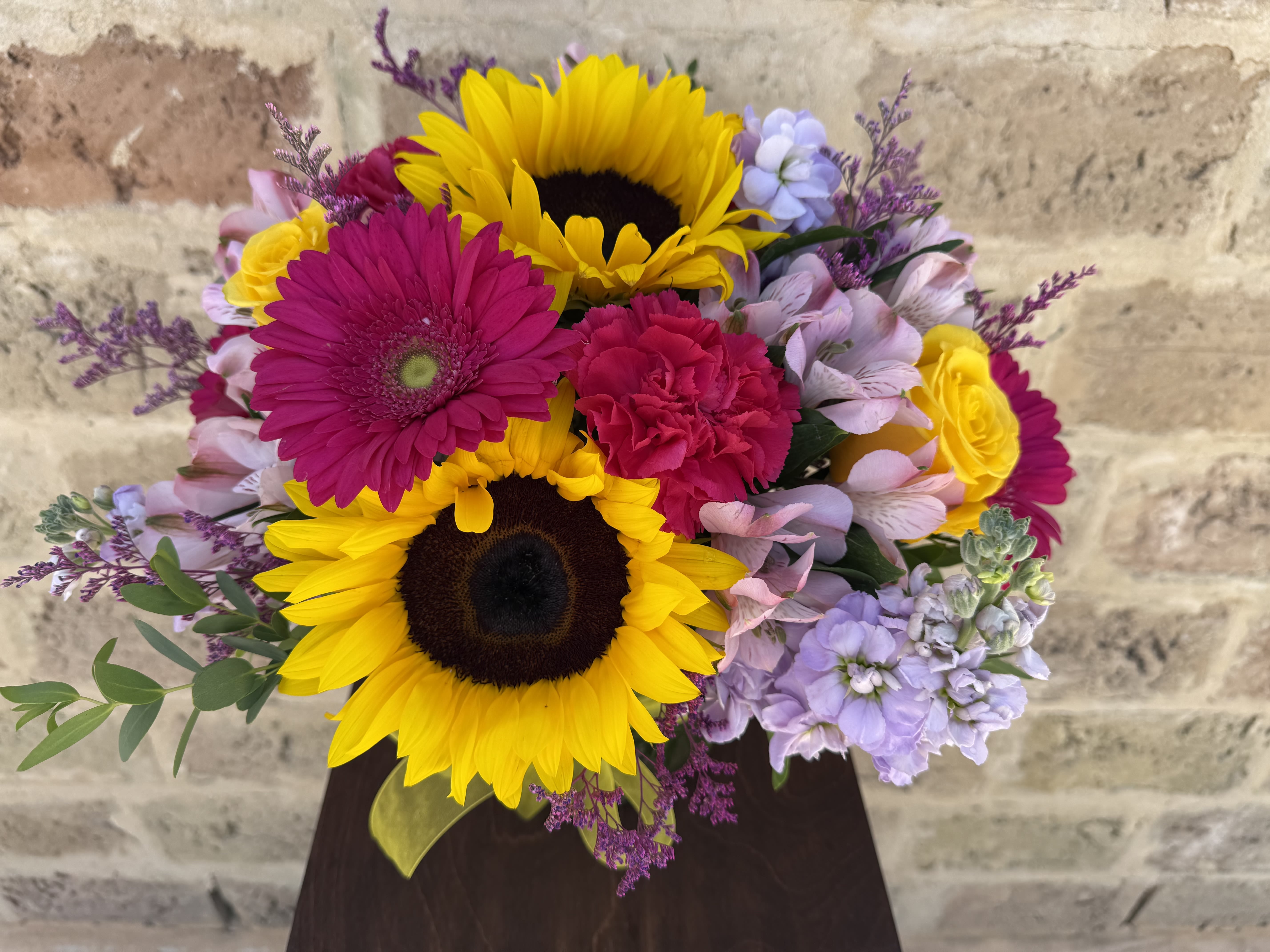 Bright mixed bouquet with sunflowers, gerbera daisies, and roses in a dark vase
