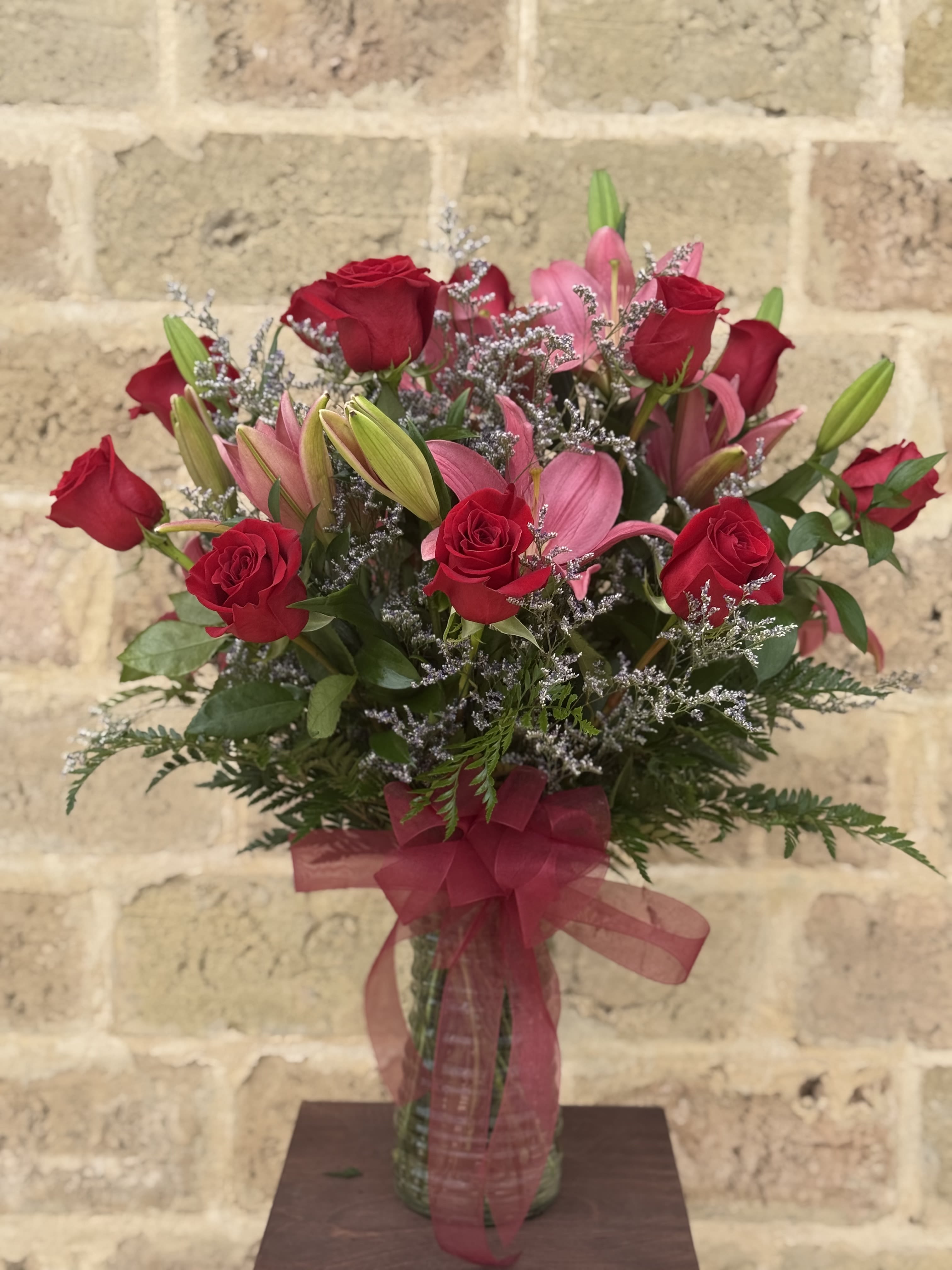 Bouquet of red roses and pink lilies in a glass vase with a ribbon