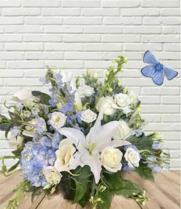 White lilies, roses, and blue flowers in a low arrangement with a butterfly accent