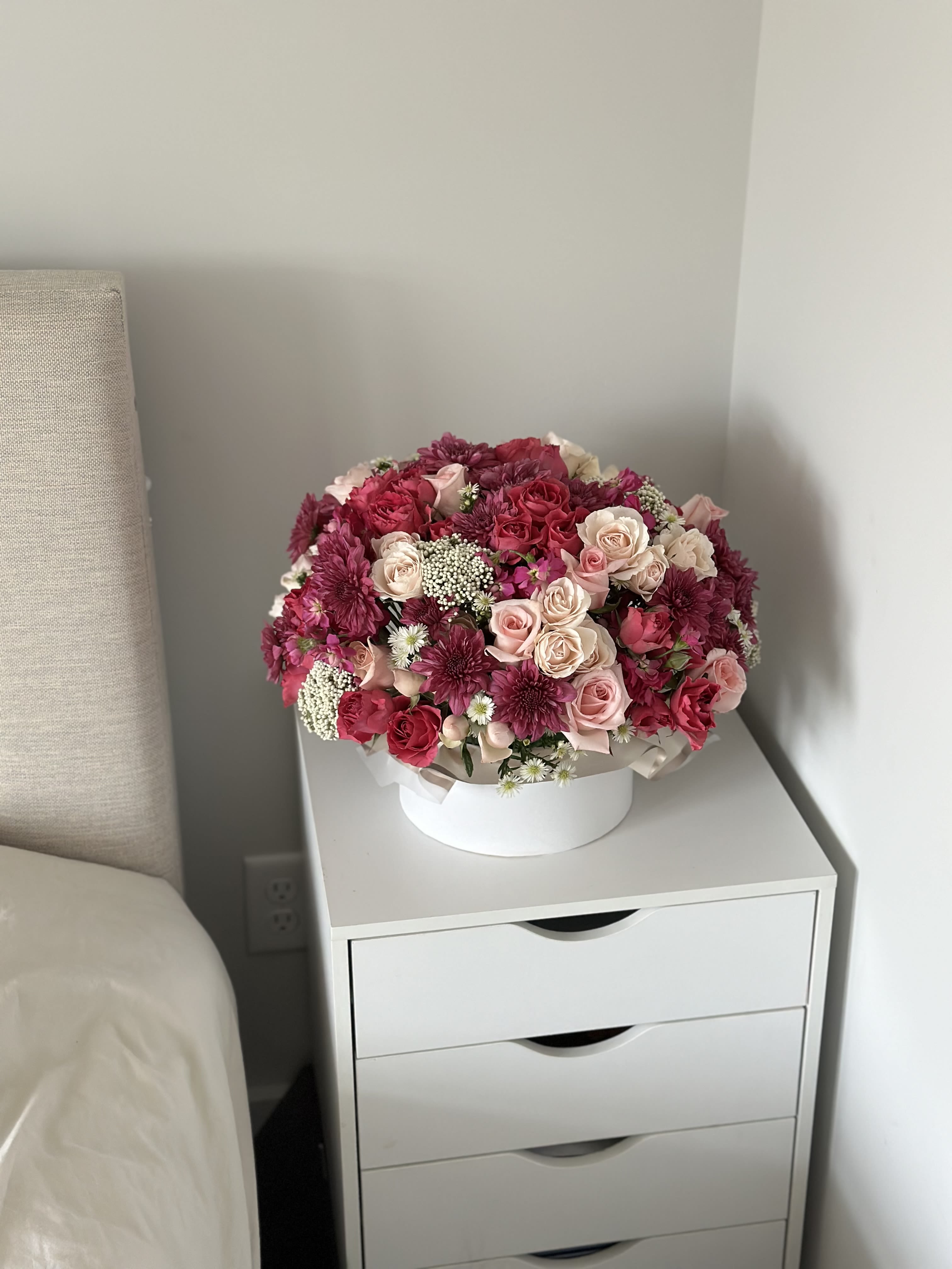 Round bouquet of pink and burgundy roses with small white filler flowers in a white box