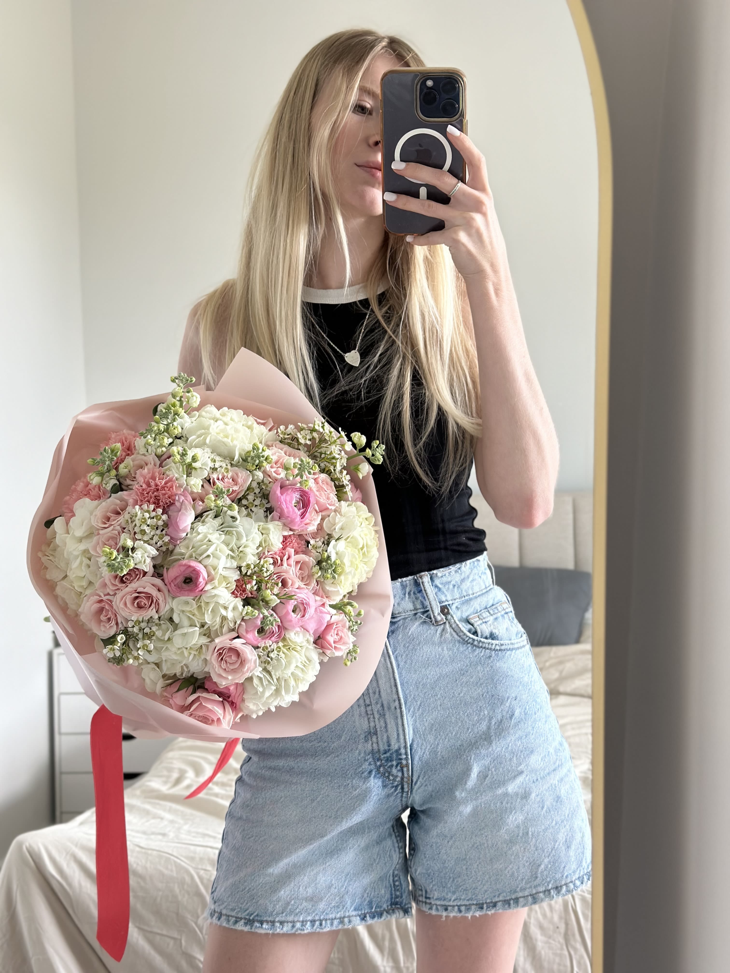Woman holding a pink and white mixed flower bouquet in front of a mirror