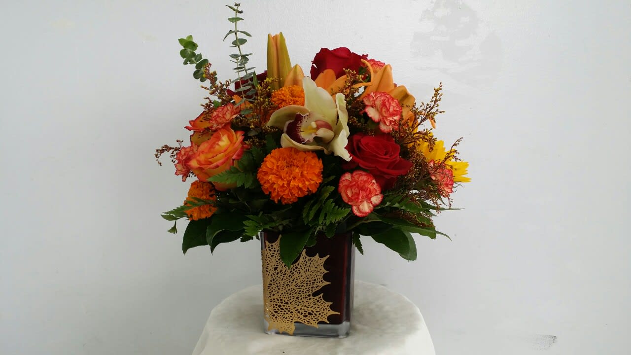 Mixed bouquet in a square glass vase with red, orange, and yellow flowers