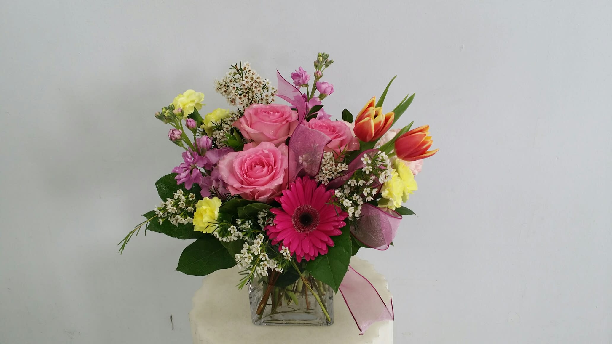 Mixed bouquet of pink roses, gerbera daisies, and tulips in a glass vase
