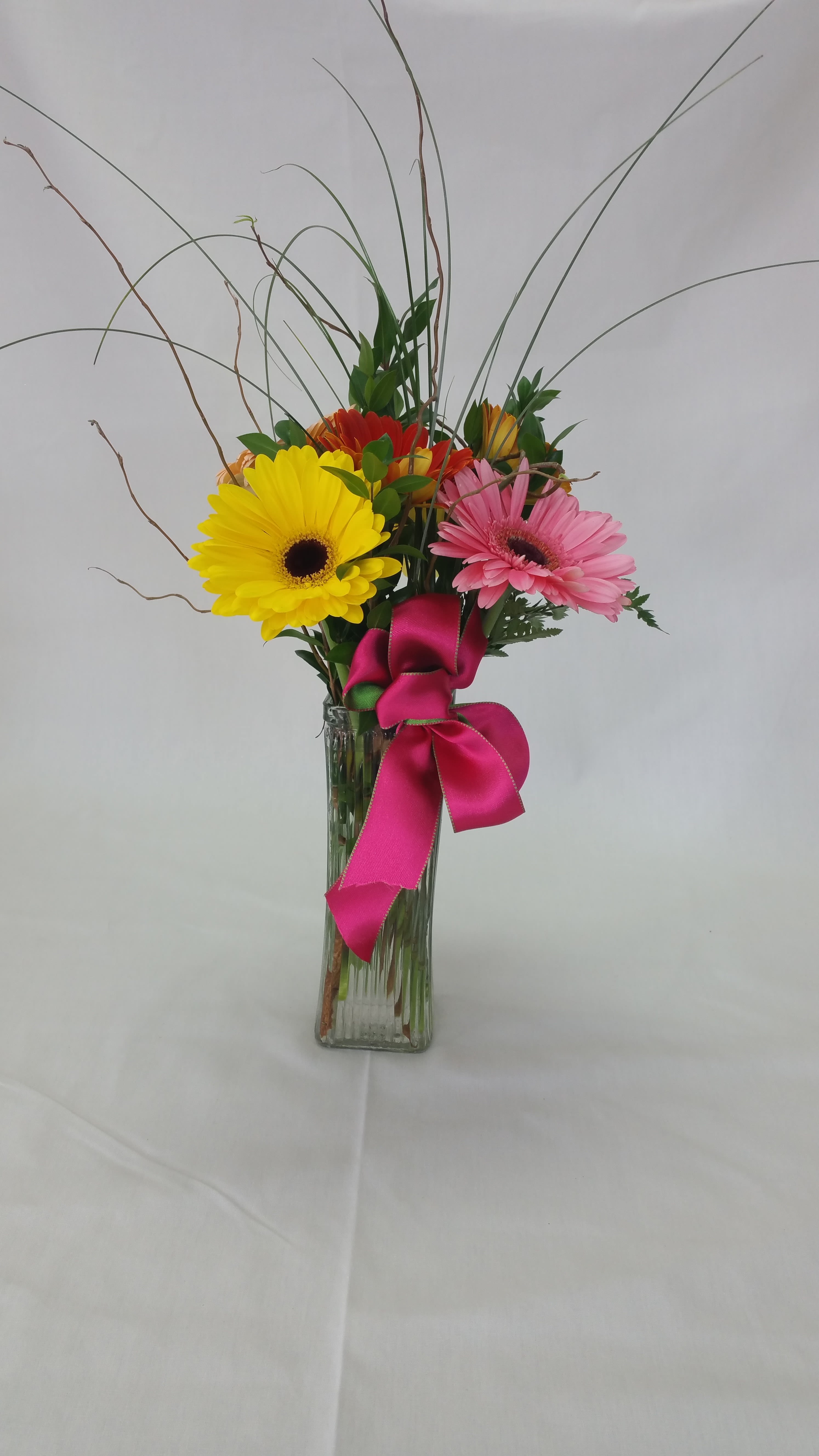 Gerbera daisies in a clear glass vase with a pink ribbon