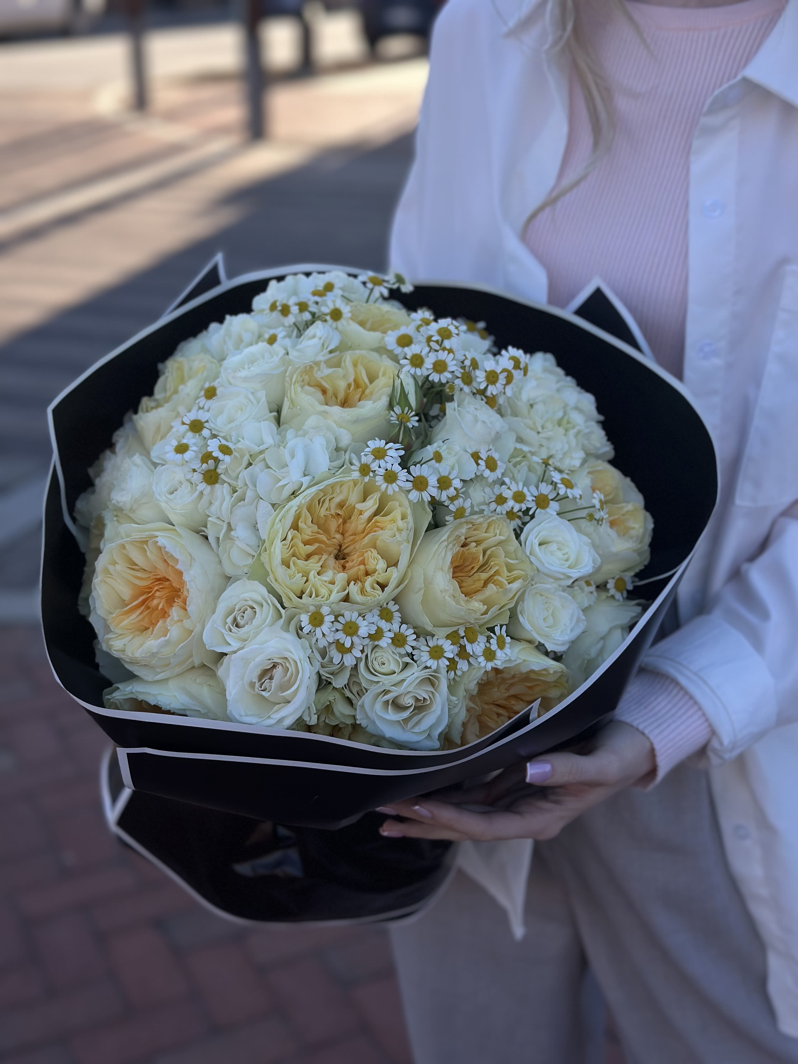 Bouquet of cream roses and small white daisies wrapped in black paper