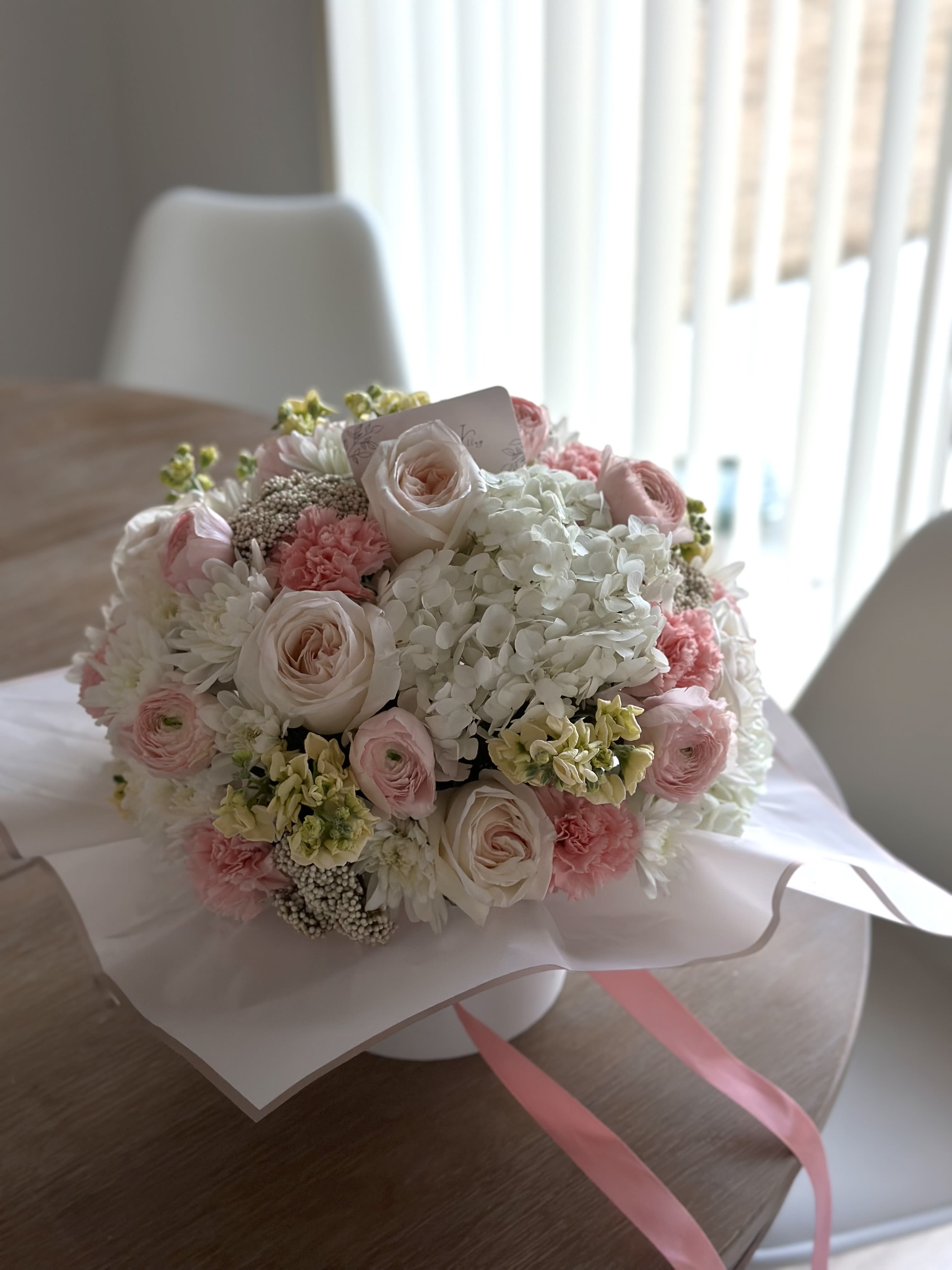 Round bouquet of pale pink and white flowers wrapped in paper
