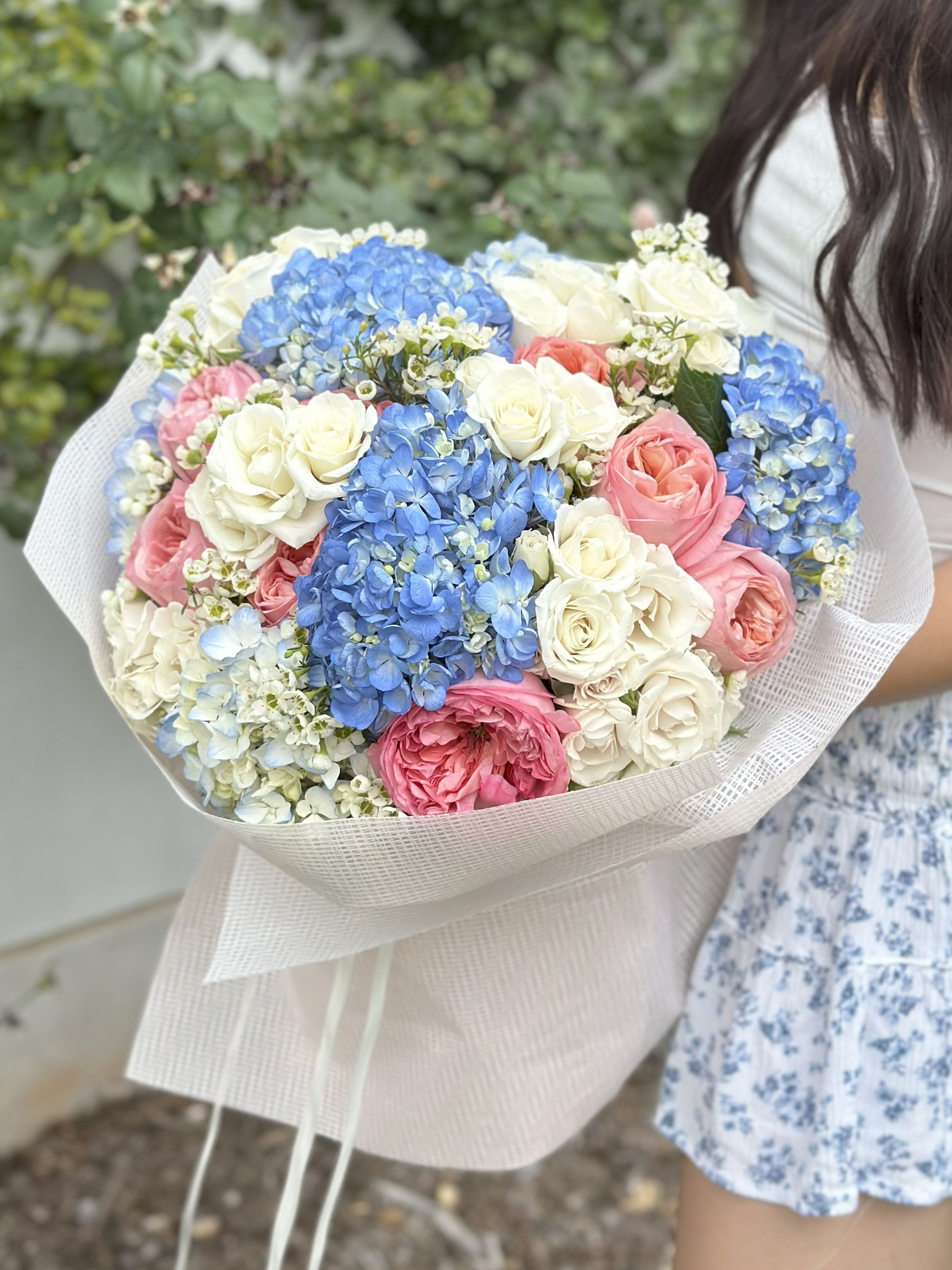 Large bouquet of blue hydrangeas and pink and white roses wrapped in pale paper