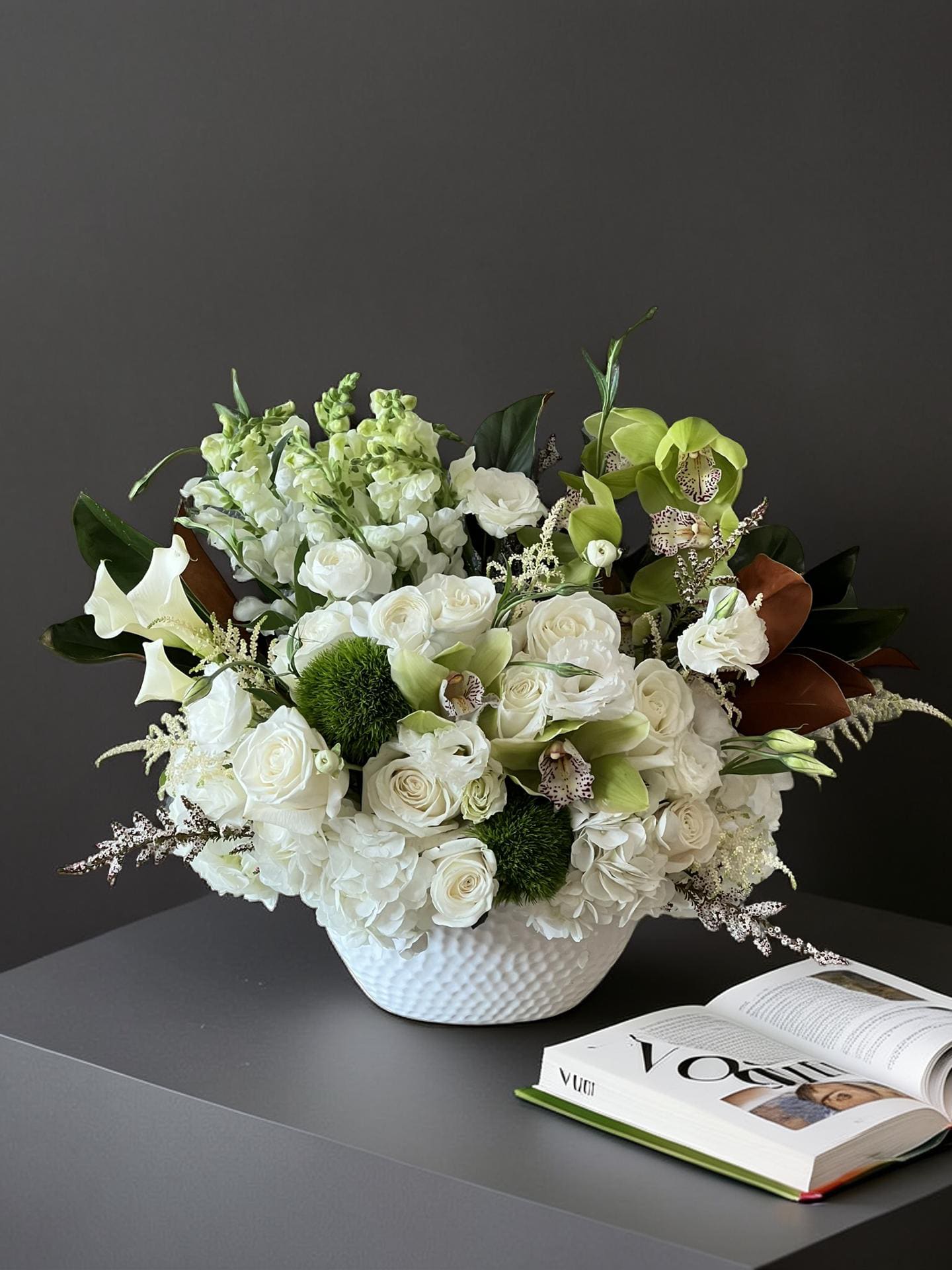 The Plaza - This elegant arrangement features a mix of fresh white flowers, including roses and hydrangeas, complemented by vibrant green orchids and other greenery, presented in a modern white bowl vase. It is designed to bring a touch of sophistication and natural beauty to any space