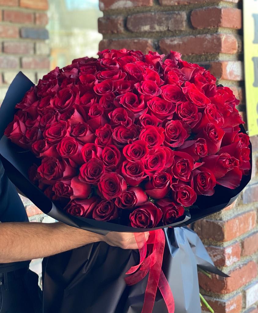 Large bouquet of red roses wrapped in black paper with a red ribbon