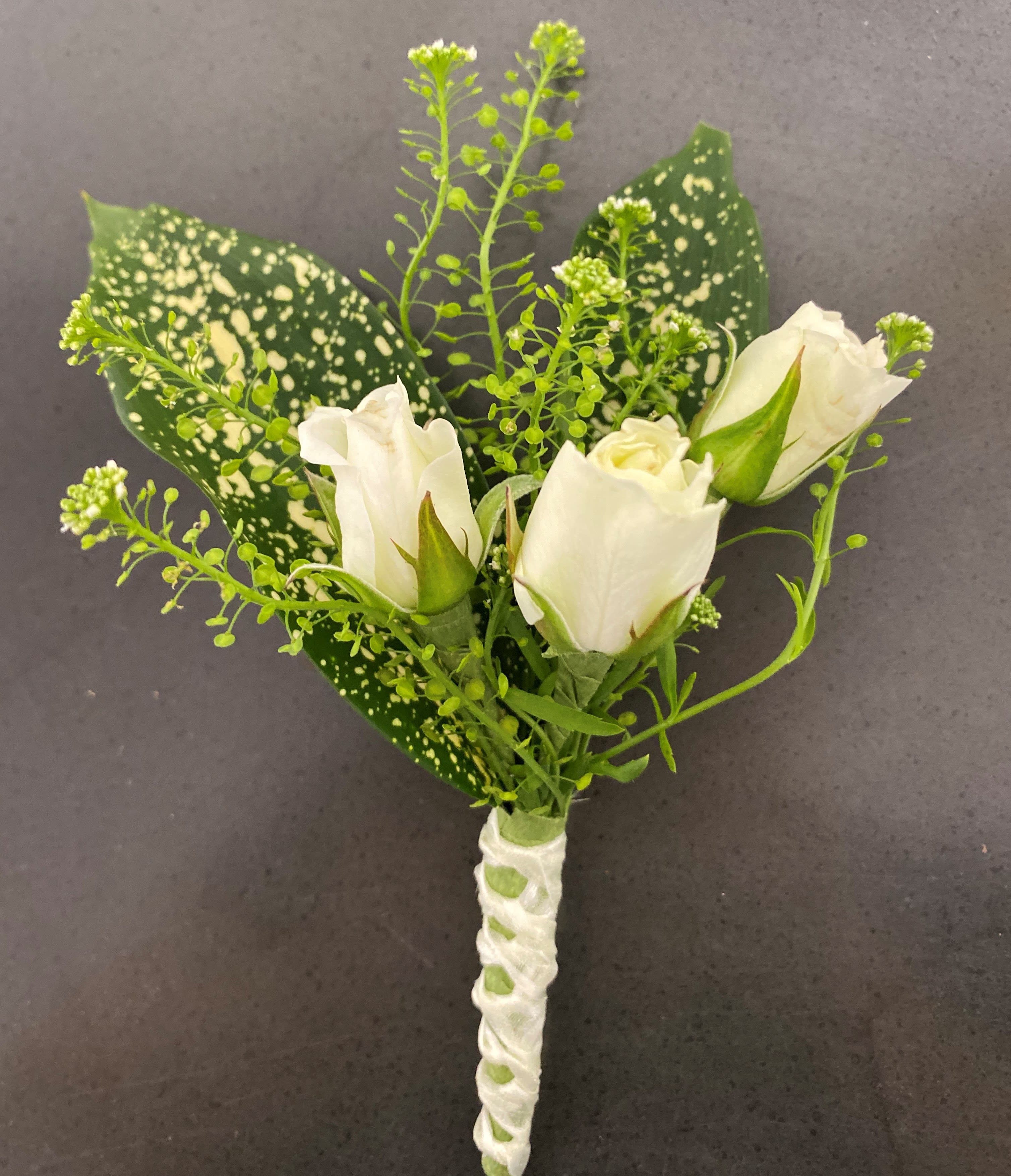 White rose boutonniere with speckled green leaves and ribbon wrap