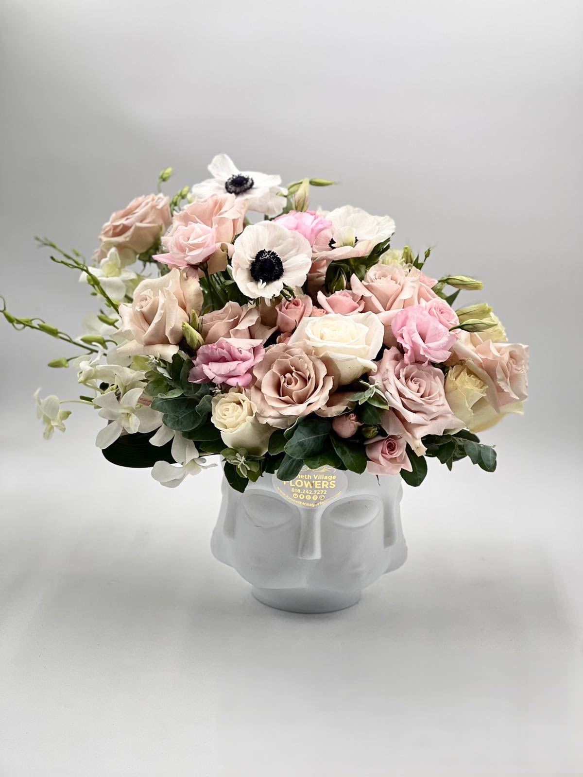Low pastel arrangement of roses, anemones, and orchids in a white ceramic face vase