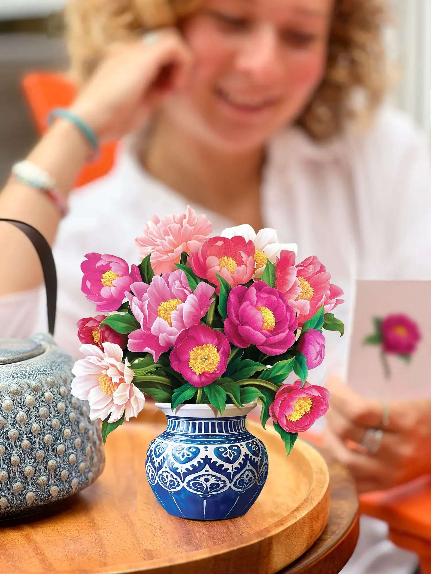 Mini Peony Paradise Pop-Up Card - Little blooms make for a big statement in the Mini Peony Paradise. Featuring a delightful assortment of rich pink hues in paper peony blossoms, our paper flower bouquet includes an indigo and white patterned pot and a matching blank notecard. Symbolic of bliss and beauty, this is the perfect arrangement to wow your loved ones with classic sentiments of love and well wishes in a dainty size.
