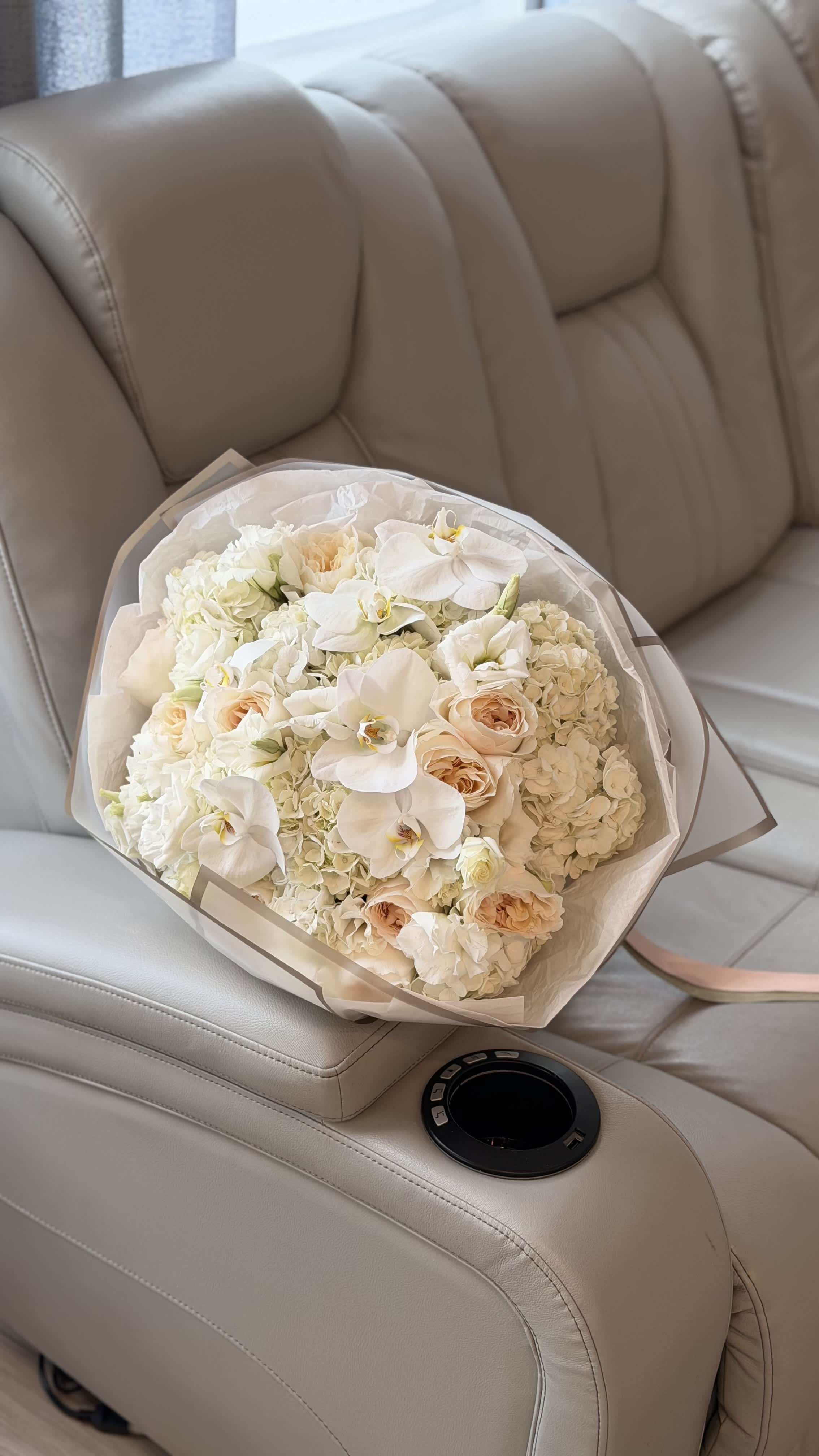 Bouquet of white orchids, cream roses, and hydrangeas wrapped in clear paper
