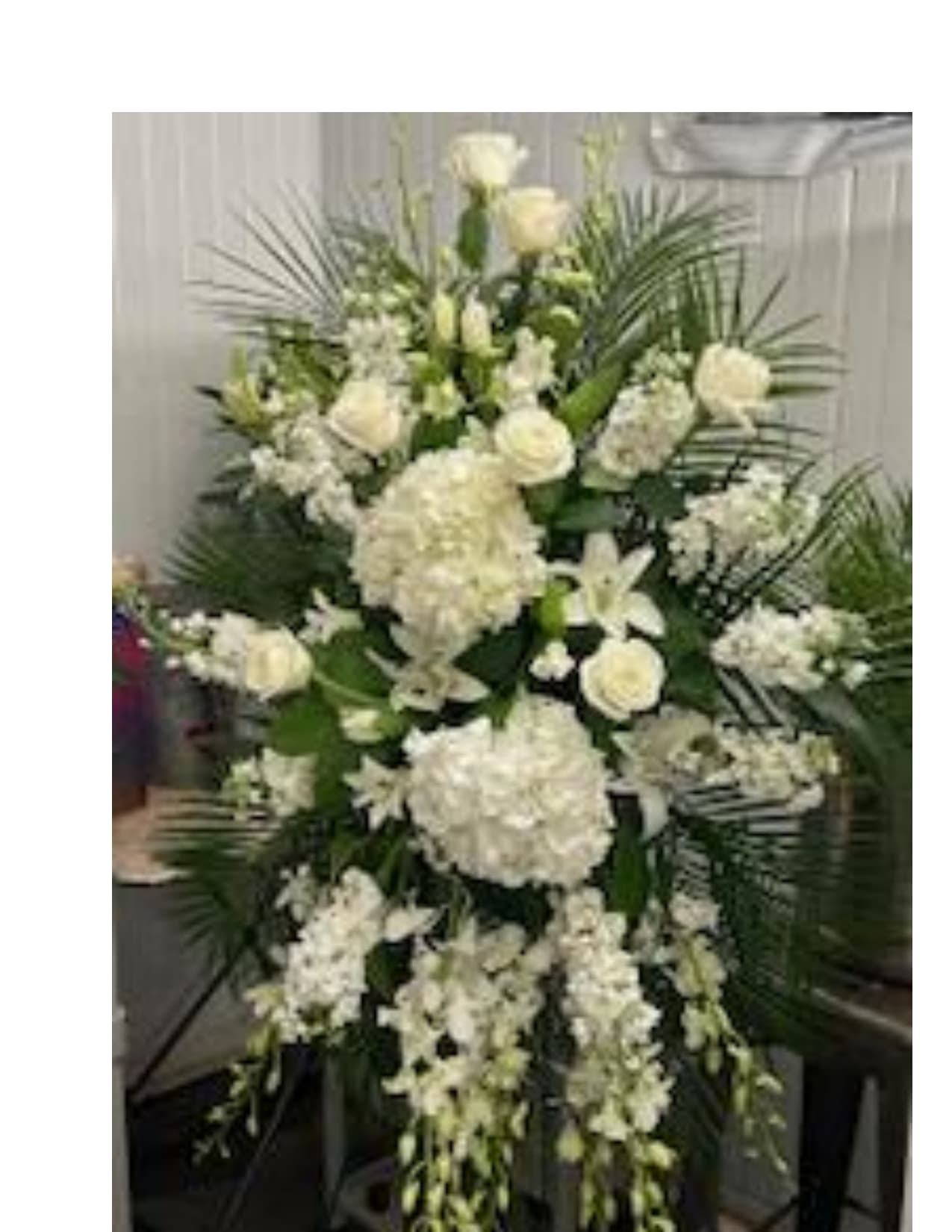Tall white funeral spray with roses, hydrangeas, and lilies