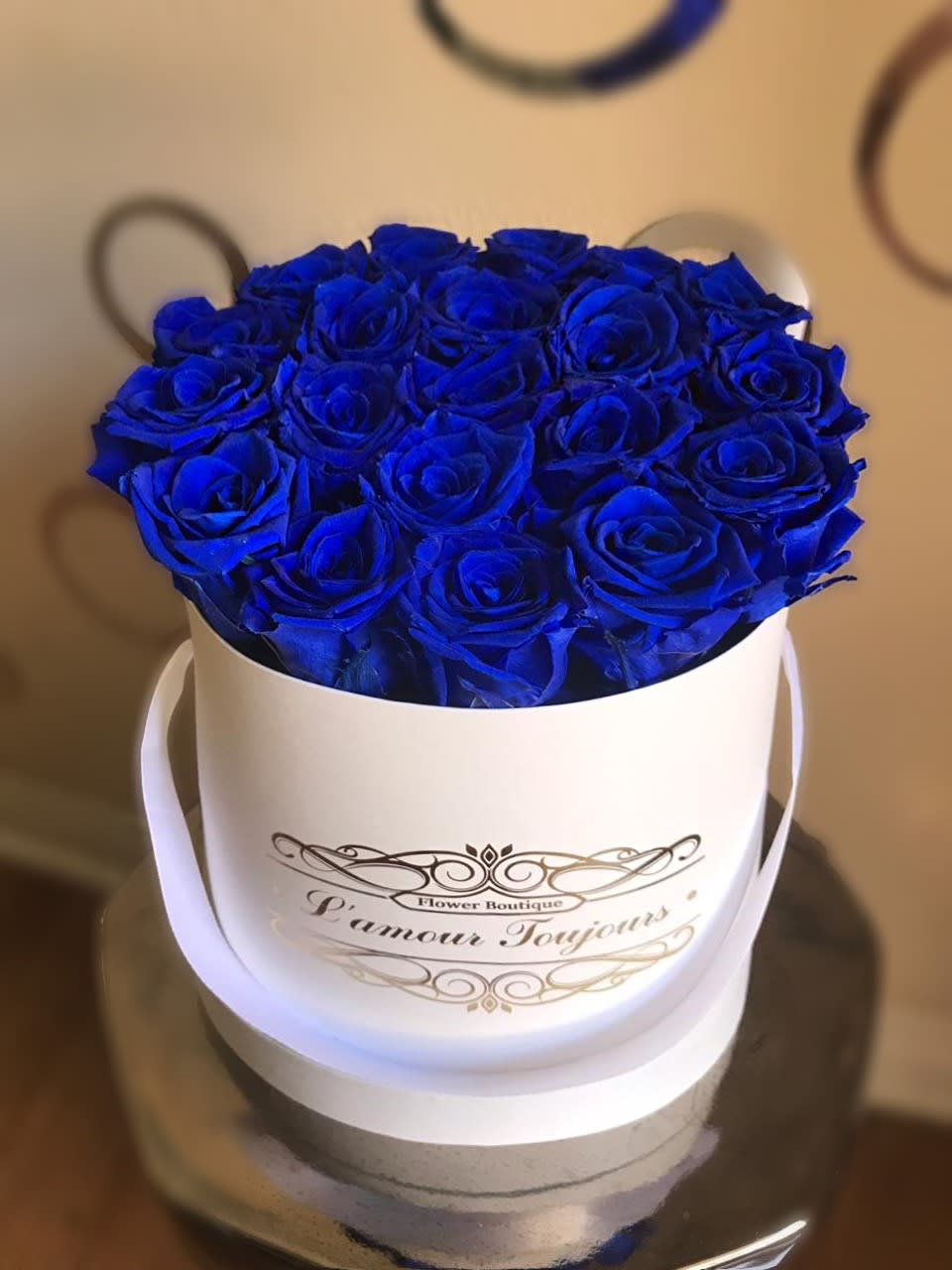 Blue roses arranged in a white round hatbox with ribbon handles