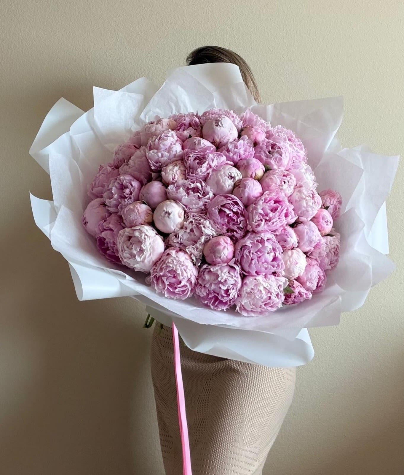 Peonies signature bouquet - Fifty blushing peonies create a cloudlike, romantic statement perfect for a birthday bouquet, anniversary roses alternative, or a Mother's Day surprise. The large, hand-tied arrangement shows blooms at varying stages of opening so the recipient will enjoy unfolding layers of soft blush and deeper rose tones-an unmistakably feminine, celebratory impression that reads as both luxurious and affectionate.  This lush bouquet is densely packed into a full, rounded shape and finished in crisp white paper with a narrow pink ribbon for a clean, airy presentation. The peonies' rounded petals and plush texture give a refined yet abundant feel; because many blooms are included, the bouquet holds its structure whether displayed in a vase or enjoyed wrapped. Ideal for anyone you want to make feel truly seen and cherished, the arrangement arrives ready to gift and instantly brightens springtime celebrations and milestone moments.