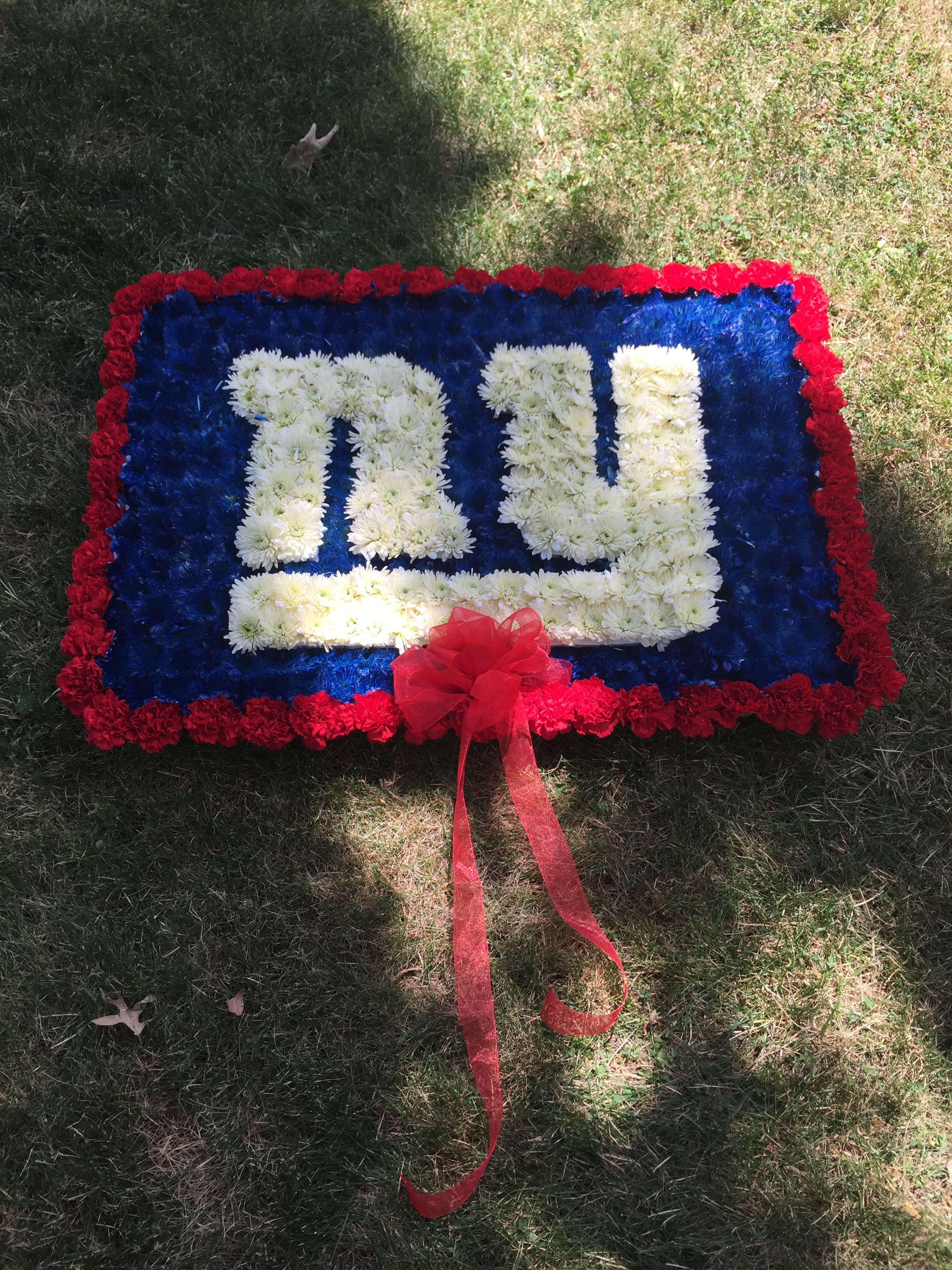 Rectangular floral tribute with white lettering, red border, and a red ribbon bow