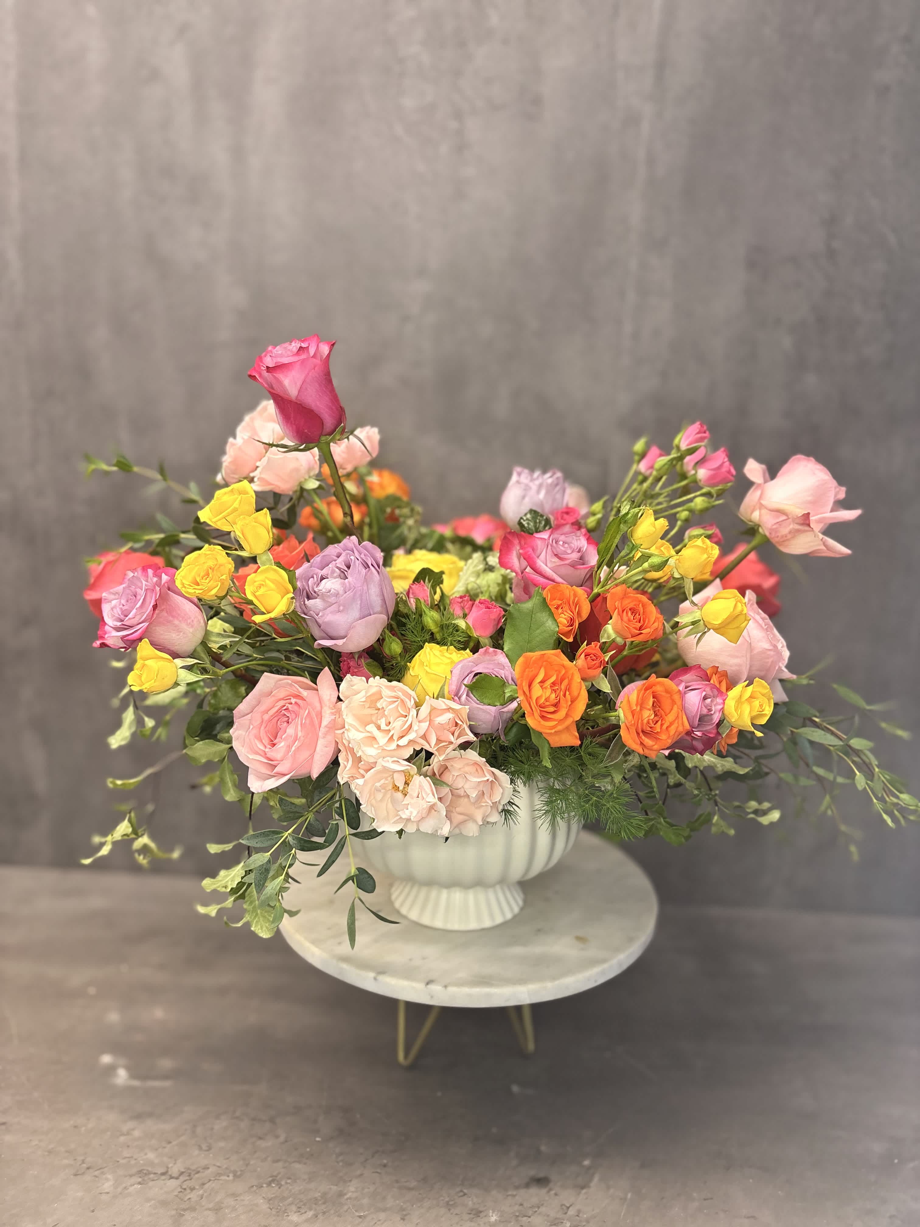 Mixed bouquet of pink, yellow, orange, and lavender roses in a white vase