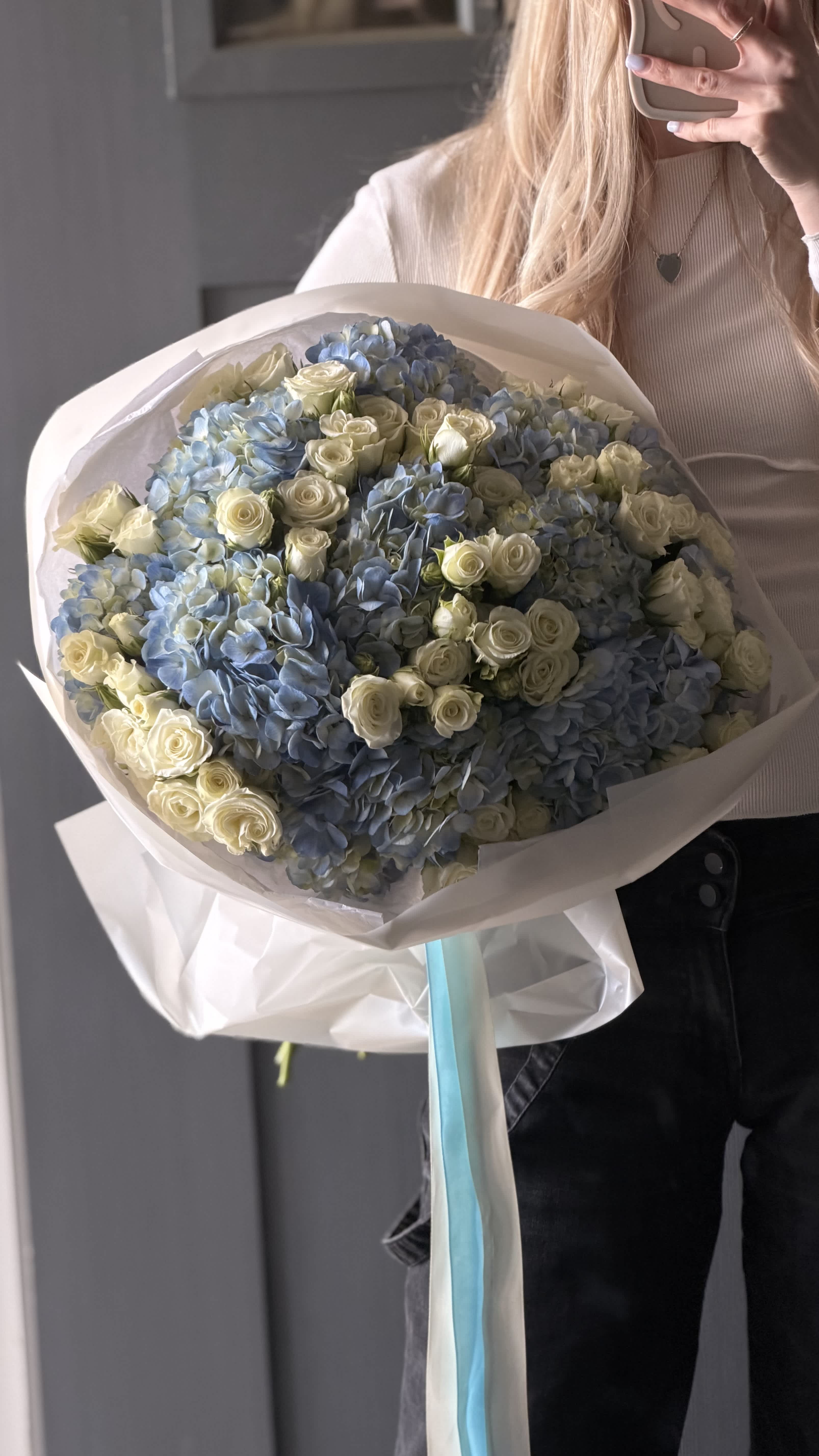 Large bouquet of blue hydrangeas and white roses wrapped in white paper