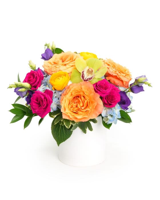Low round arrangement of orange roses and bright mixed blooms in a white cylinder vase