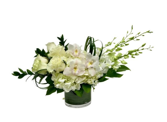Low white rose and orchid arrangement with hydrangea in a clear glass cylinder vase
