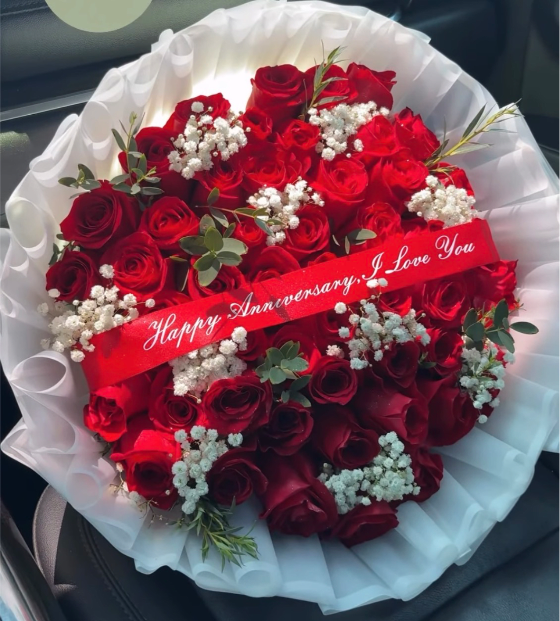 YOURS TRULY - Deep, velvety red roses clustered tight against clouds of white baby's breath create an immediate romantic statement in this anniversary flower arrangement. As a hand-tied bouquet for an anniversary or love-themed gift, YOURS TRULY pairs classic red-and-white contrast with fresh greenery so the person you're celebrating feels cherished and seen the moment they open it.  Wrapped in layered white paper and finished with a red satin ribbon that reads "Happy Anniversary, I Love You," this arrangement is compact and dense for strong visual impact. The mix of long-stem red roses, delicate white baby's breath, and small sprigs of green foliage gives texture and depth while keeping the focus on the roses' rich color.  Perfect for anniversaries, proposal celebrations, or any moment you want to say "I love you" with timeless romance, YOURS TRULY arrives ready to gift in its hand-bouquet presentation. Handled with care, keep stems in fresh water and out of direct sunlight to prolong bloom life after delivery.