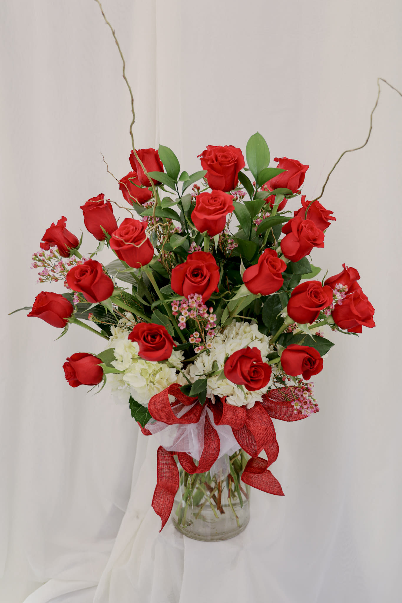 Red roses and white hydrangeas arranged in a glass vase with a red ribbon.