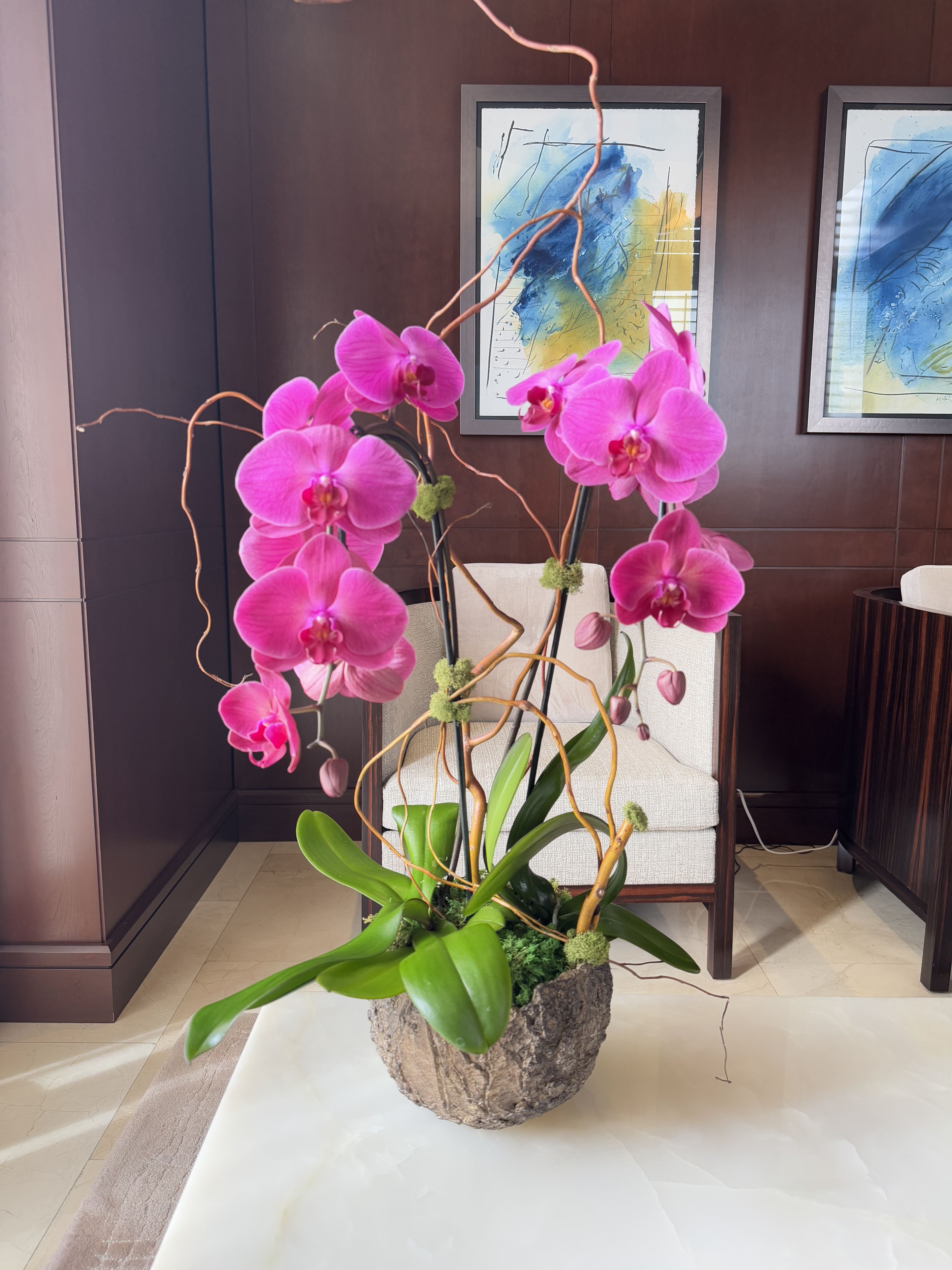 Pink orchids arranged in a decorative planter with twisting branches.