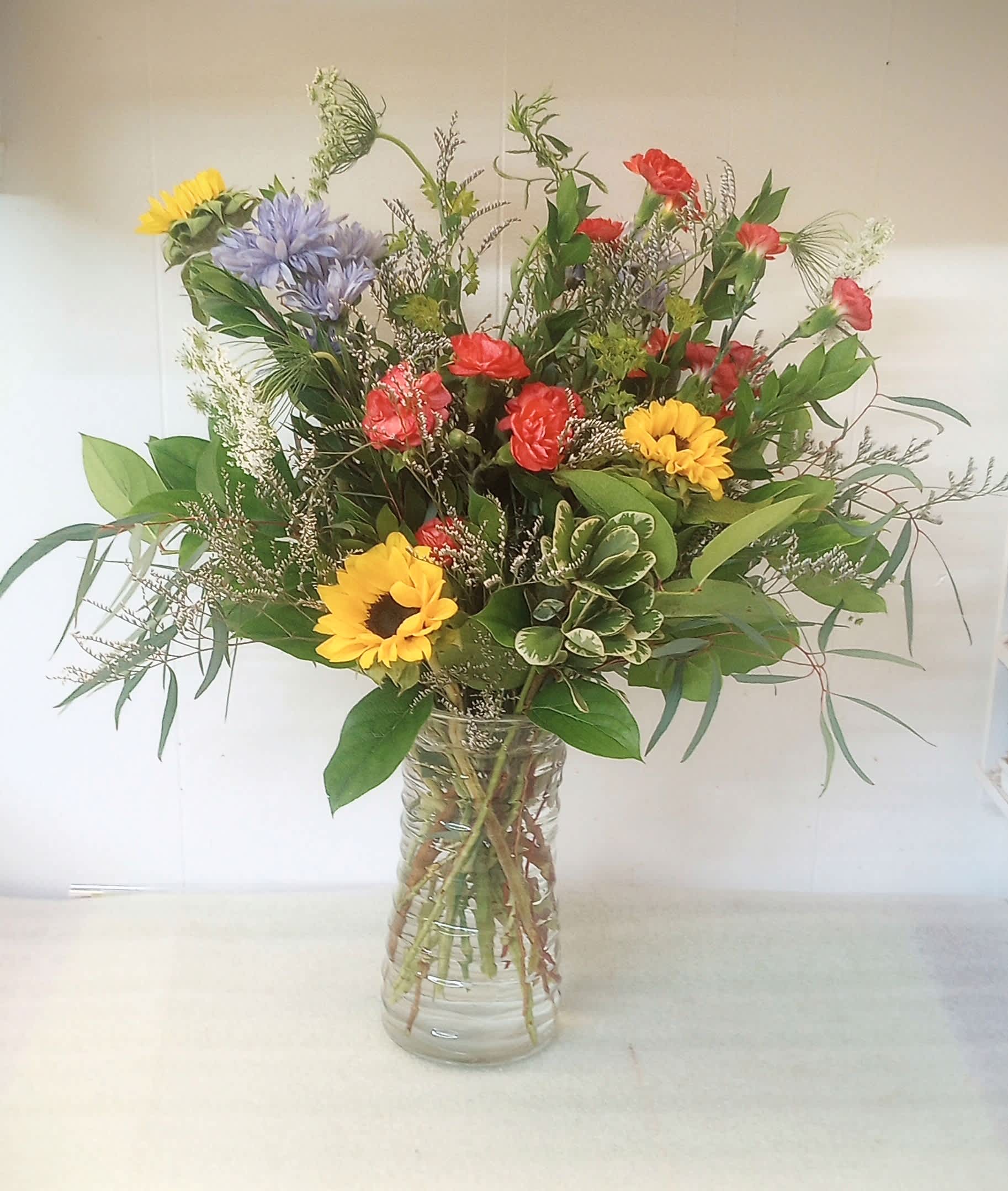 Mixed bouquet of sunflowers, red carnations, and purple blooms in a glass vase