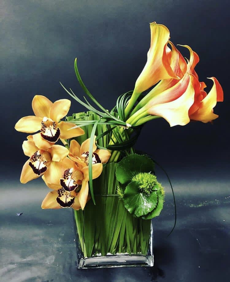 Orange calla lilies and orchids arranged in a clear glass vase