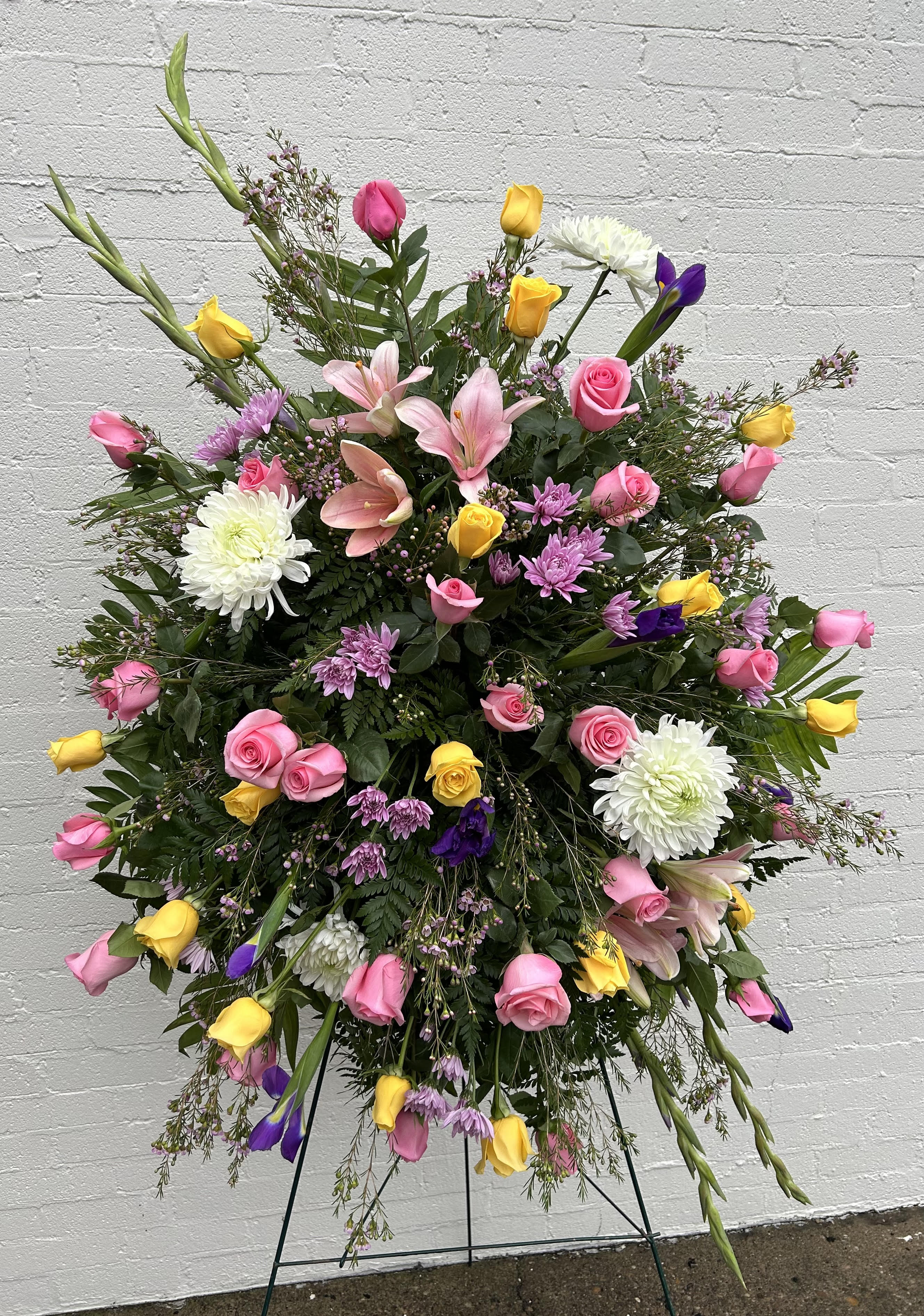 Pink Comfort Standing Spray  - Pink and yellow roses, white mums, purple iris, purple waxflower and lavender daisies.  Arrives on an easel. Appropriate for funeral home and gravesite. 