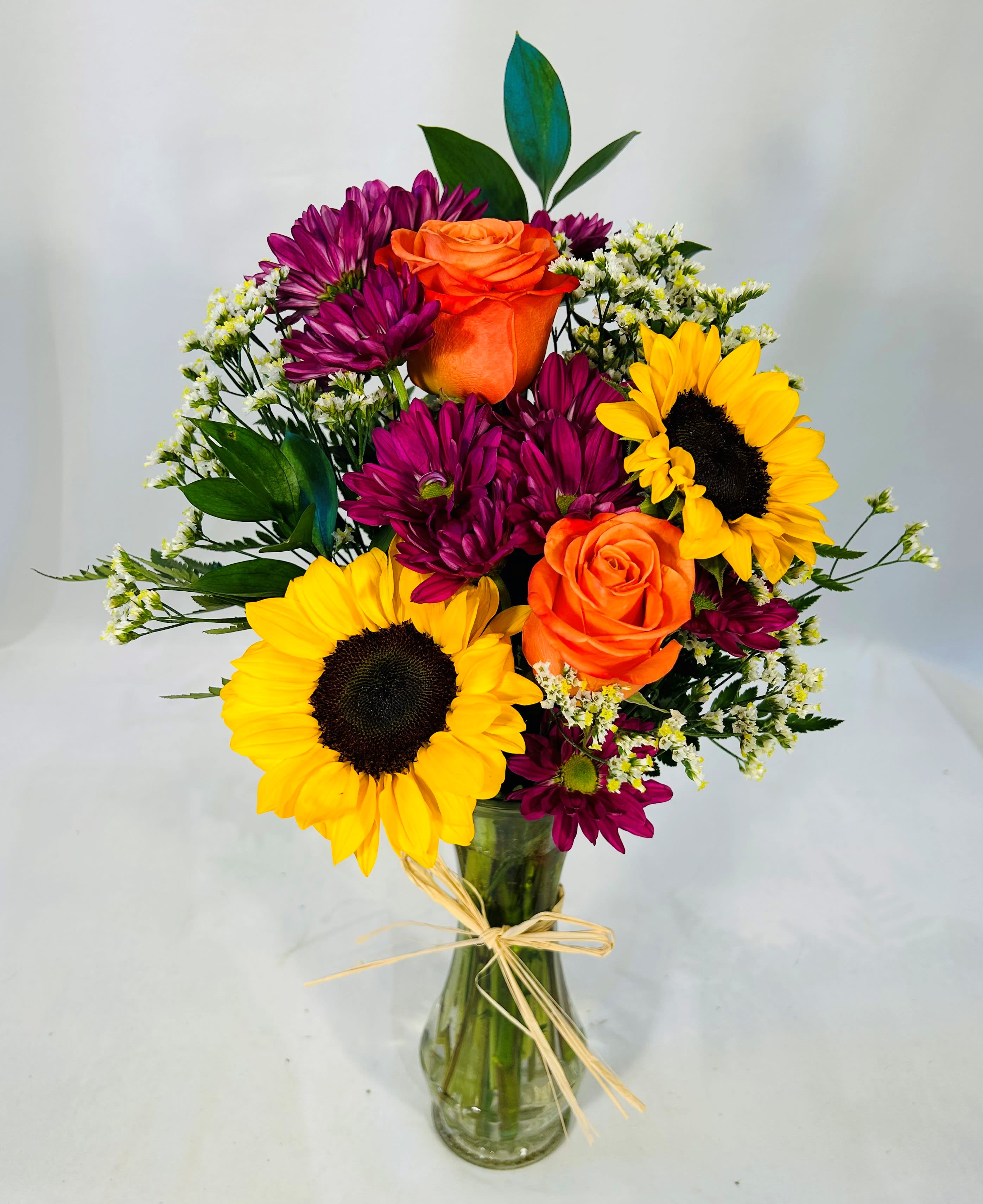 Bouquet of sunflowers, orange roses, and purple daisies in a glass vase