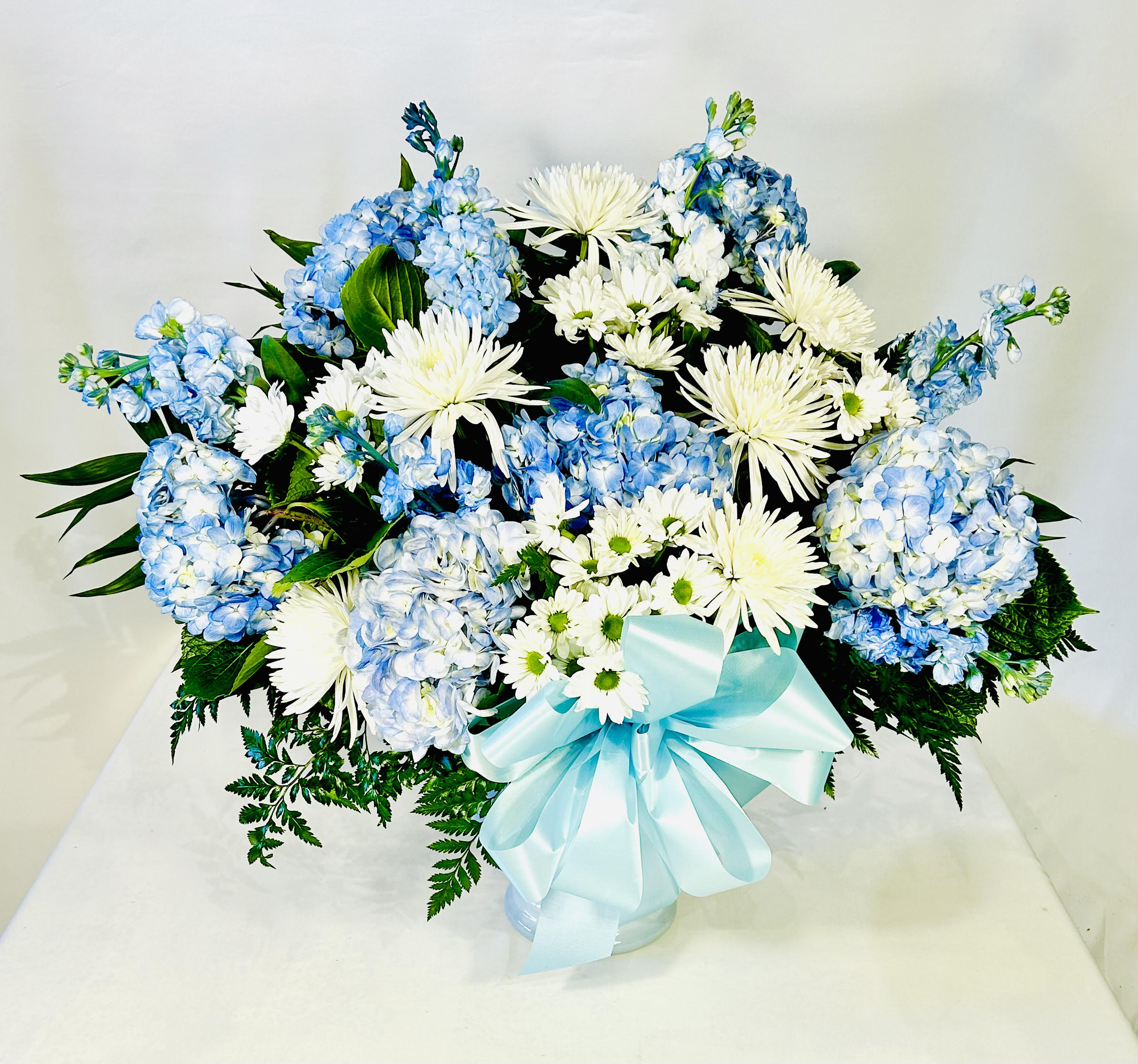 Blue hydrangeas and white chrysanthemums in a vase with a pale blue ribbon