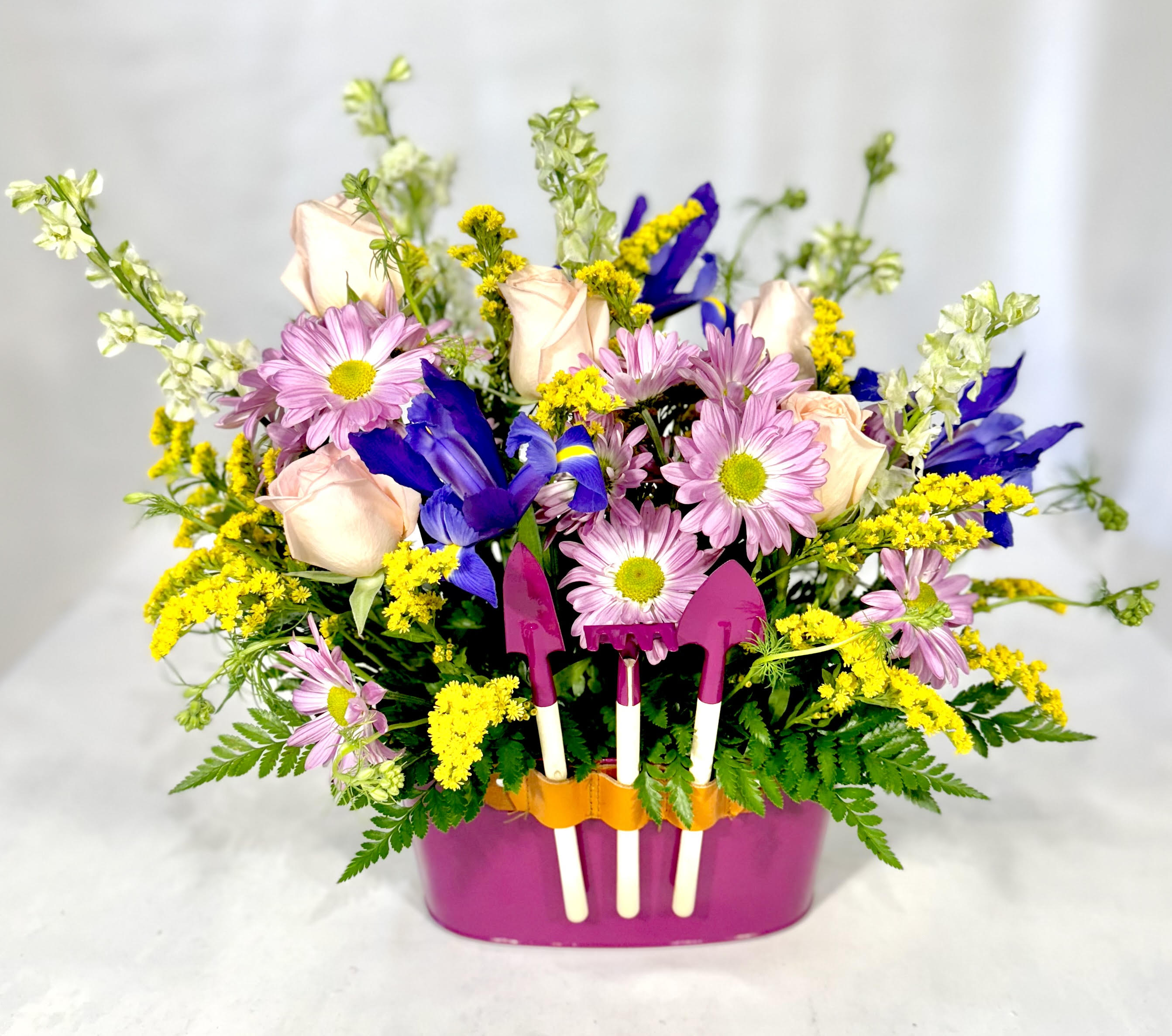 Mixed bouquet in a pink container with small garden tools