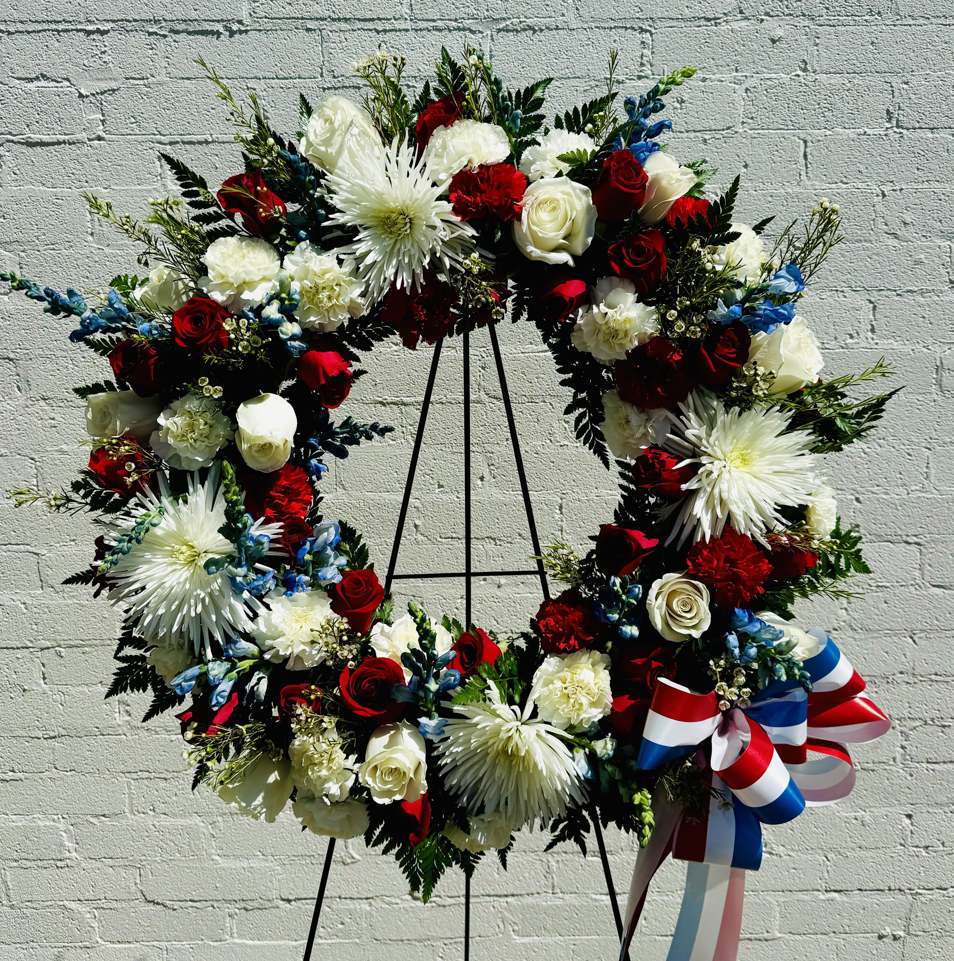 Large red, white, and blue floral wreath on a stand with ribbon