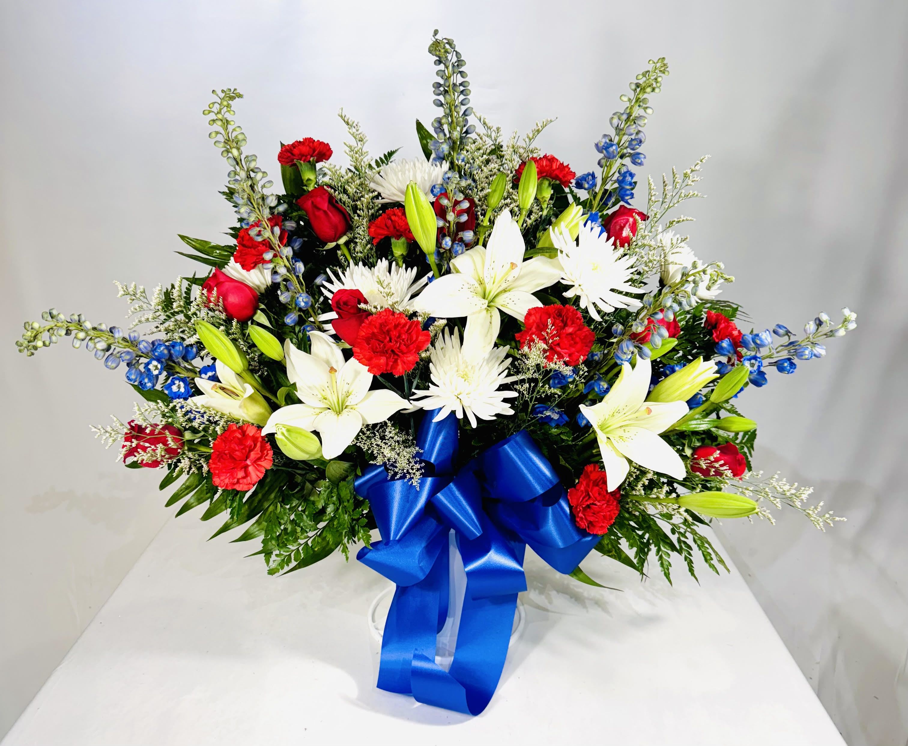 Red and white floral arrangement with a blue ribbon in a clear vase