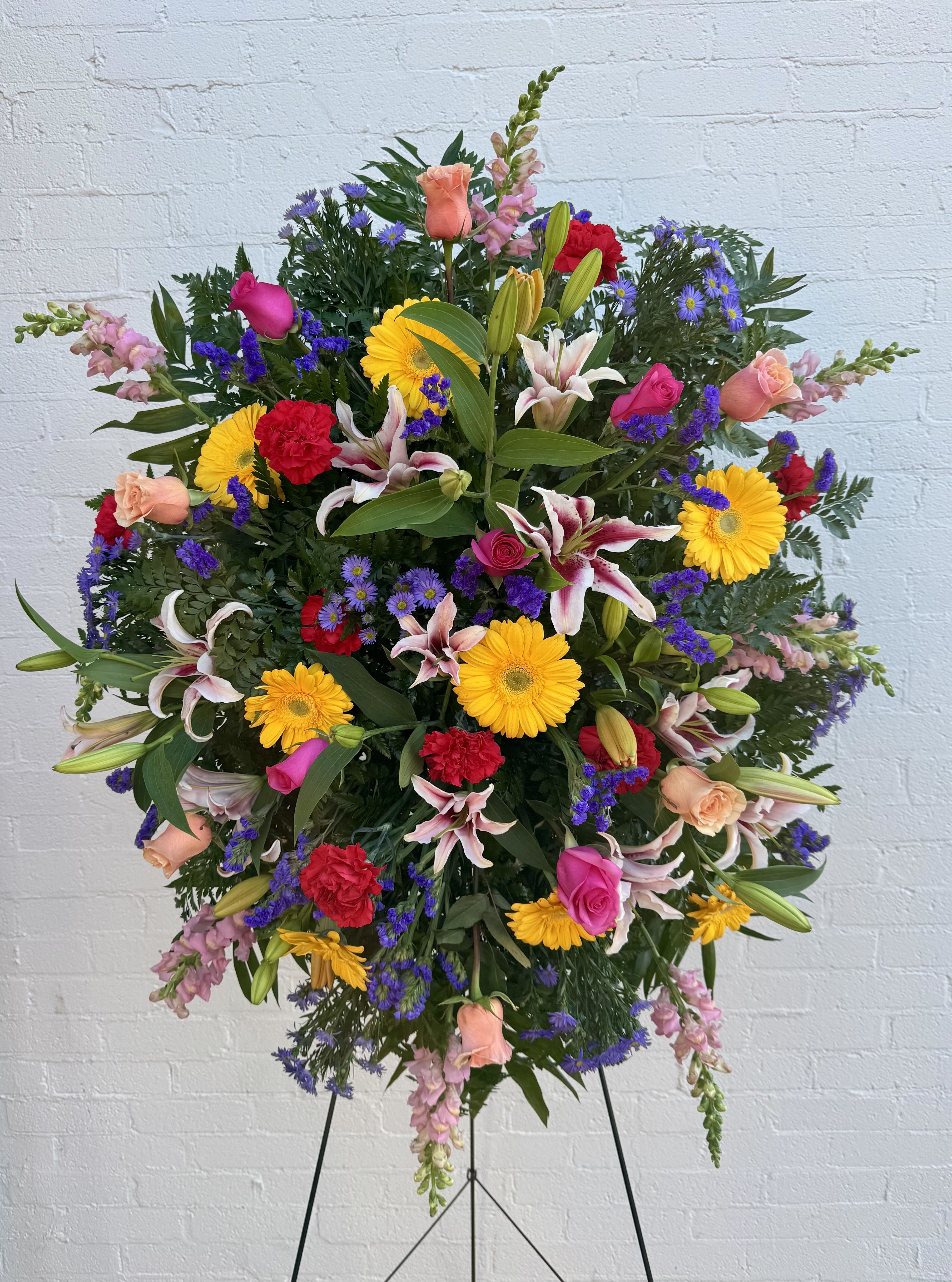 Large standing floral spray with mixed bright flowers on a black easel