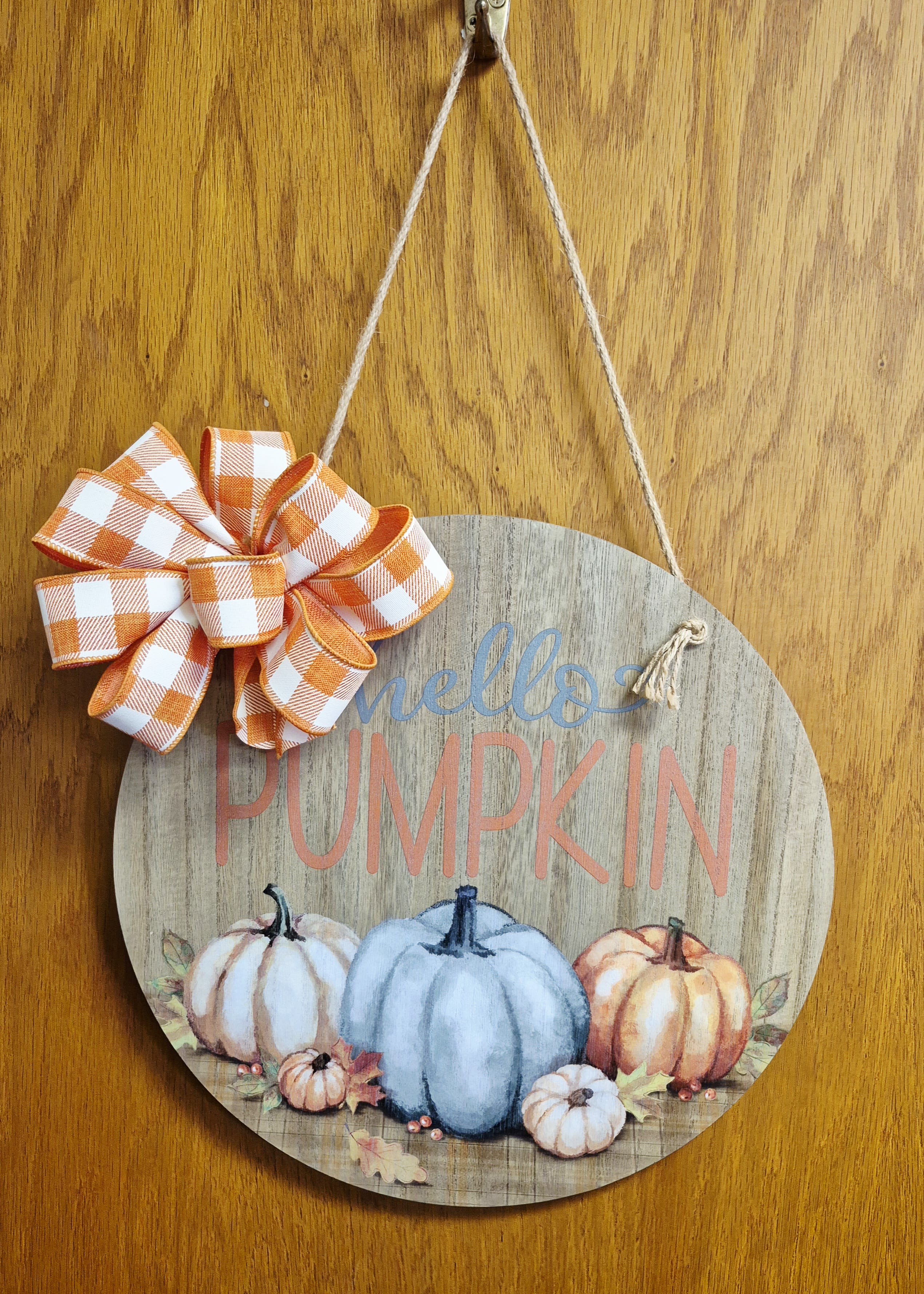 Round wooden pumpkin sign with orange plaid bow hanging by twine