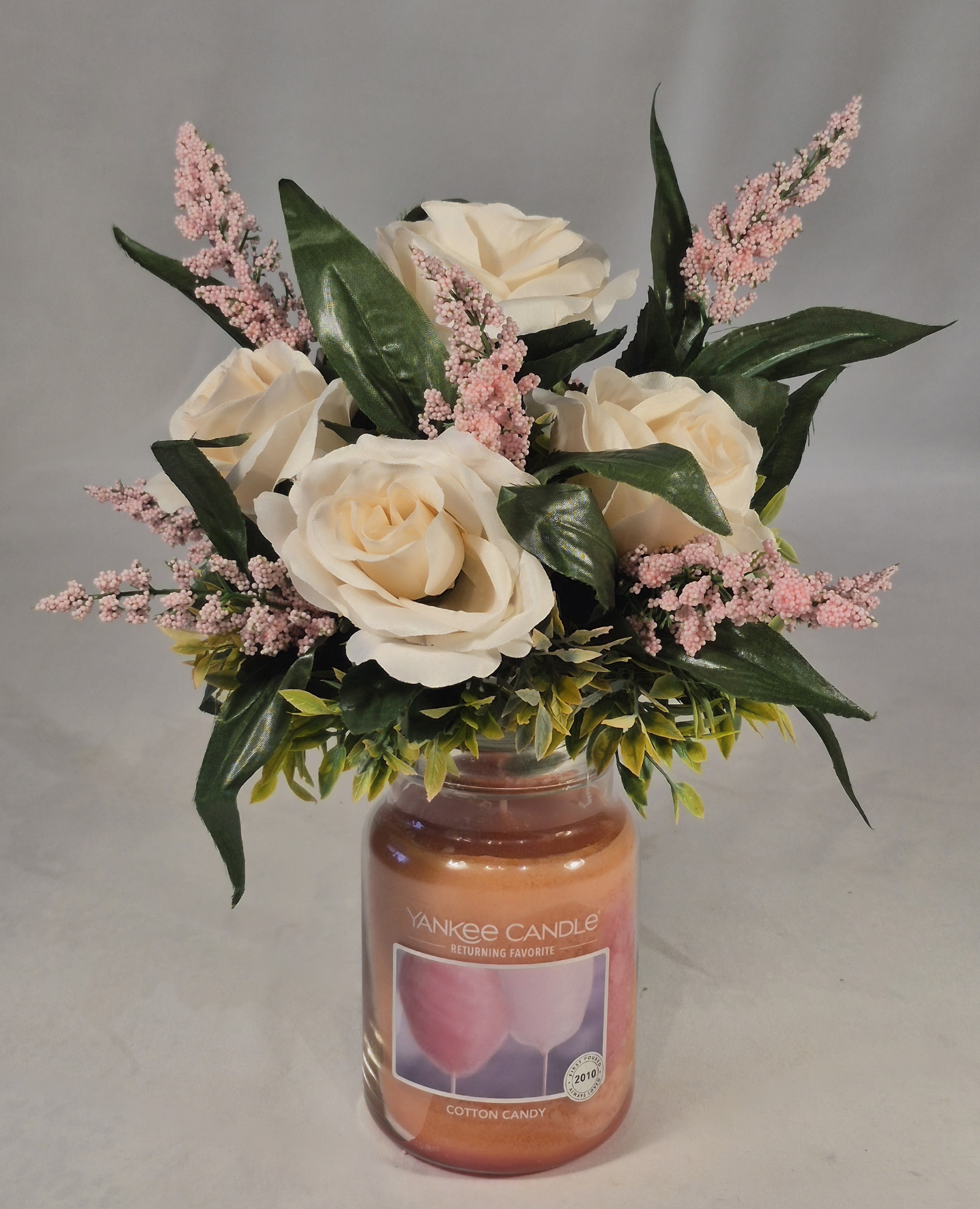 Cream roses and pink filler flowers arranged in a candle jar
